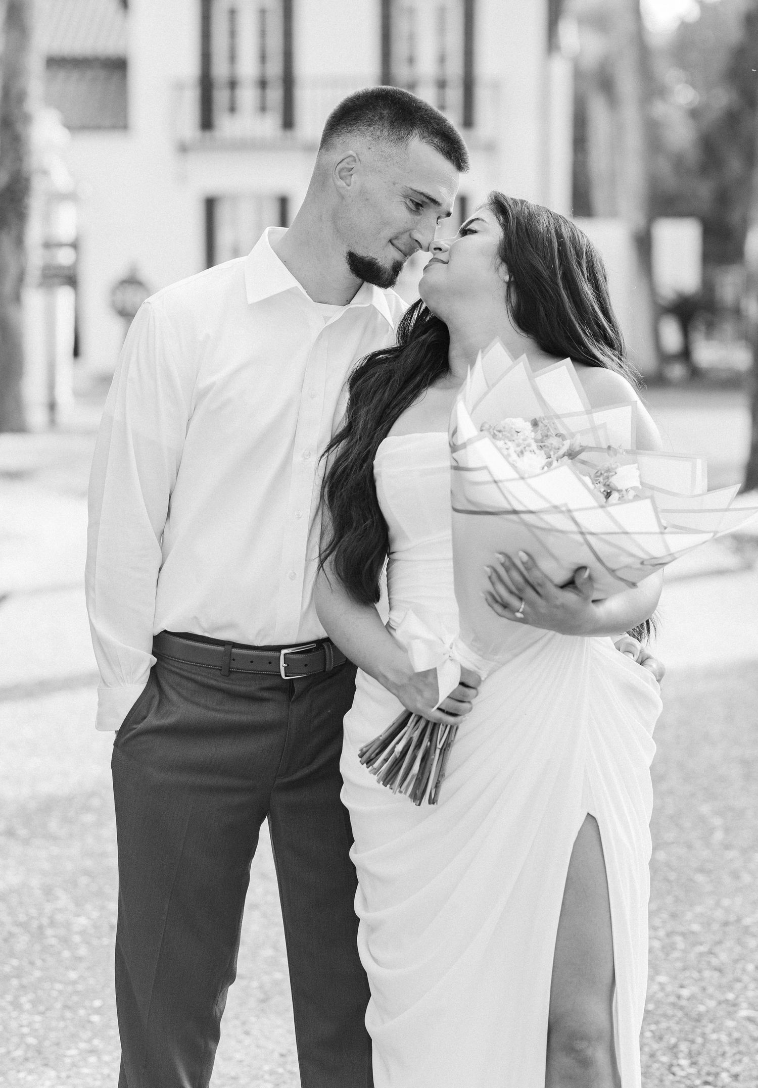 Black and white photo of a couple in wedding attire gazing at each other while the bride holds a bouquet outdoors.