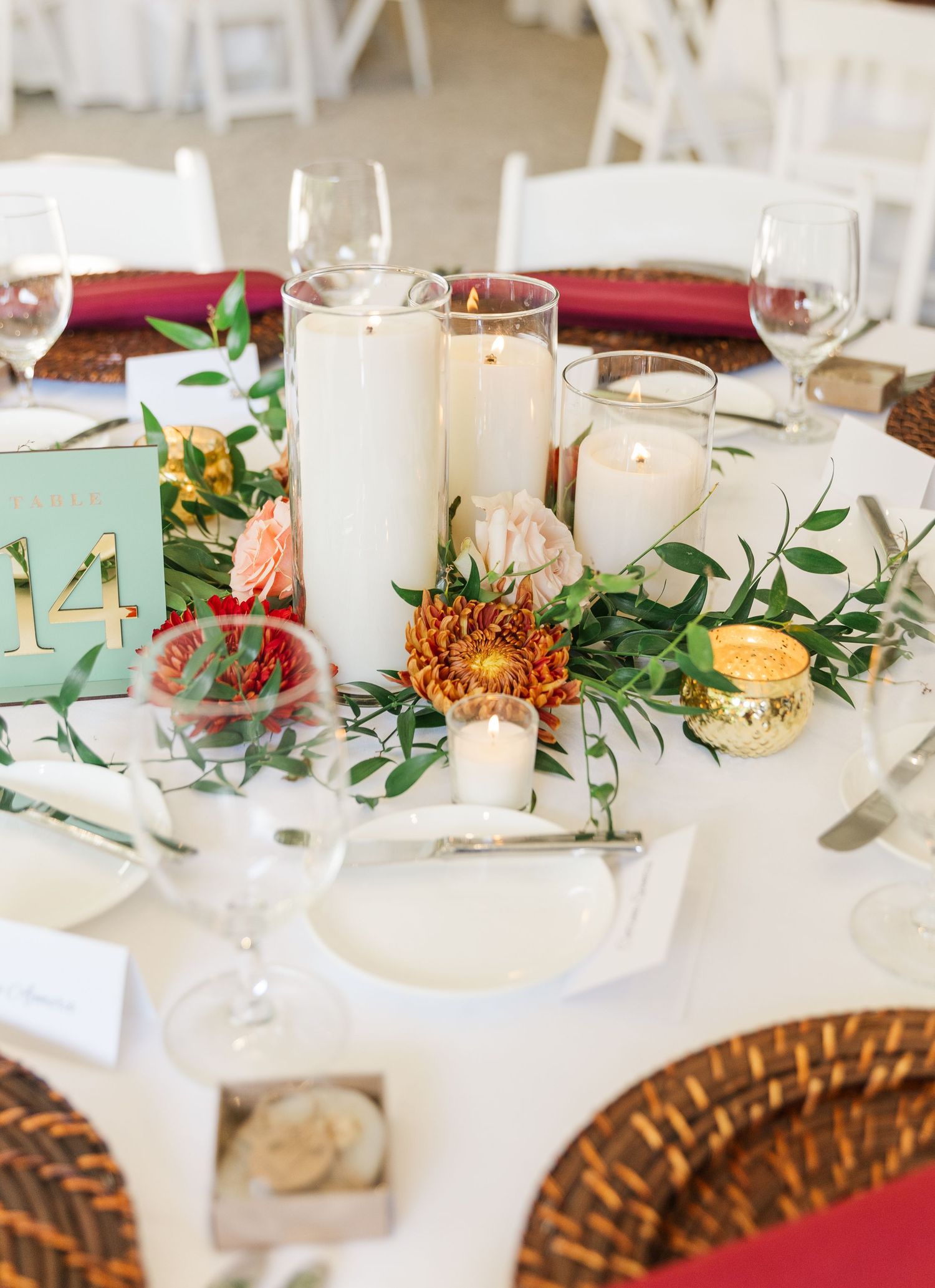 Elegant wedding reception table setting with white candles, greenery garland, and gold charger plates on white linens.