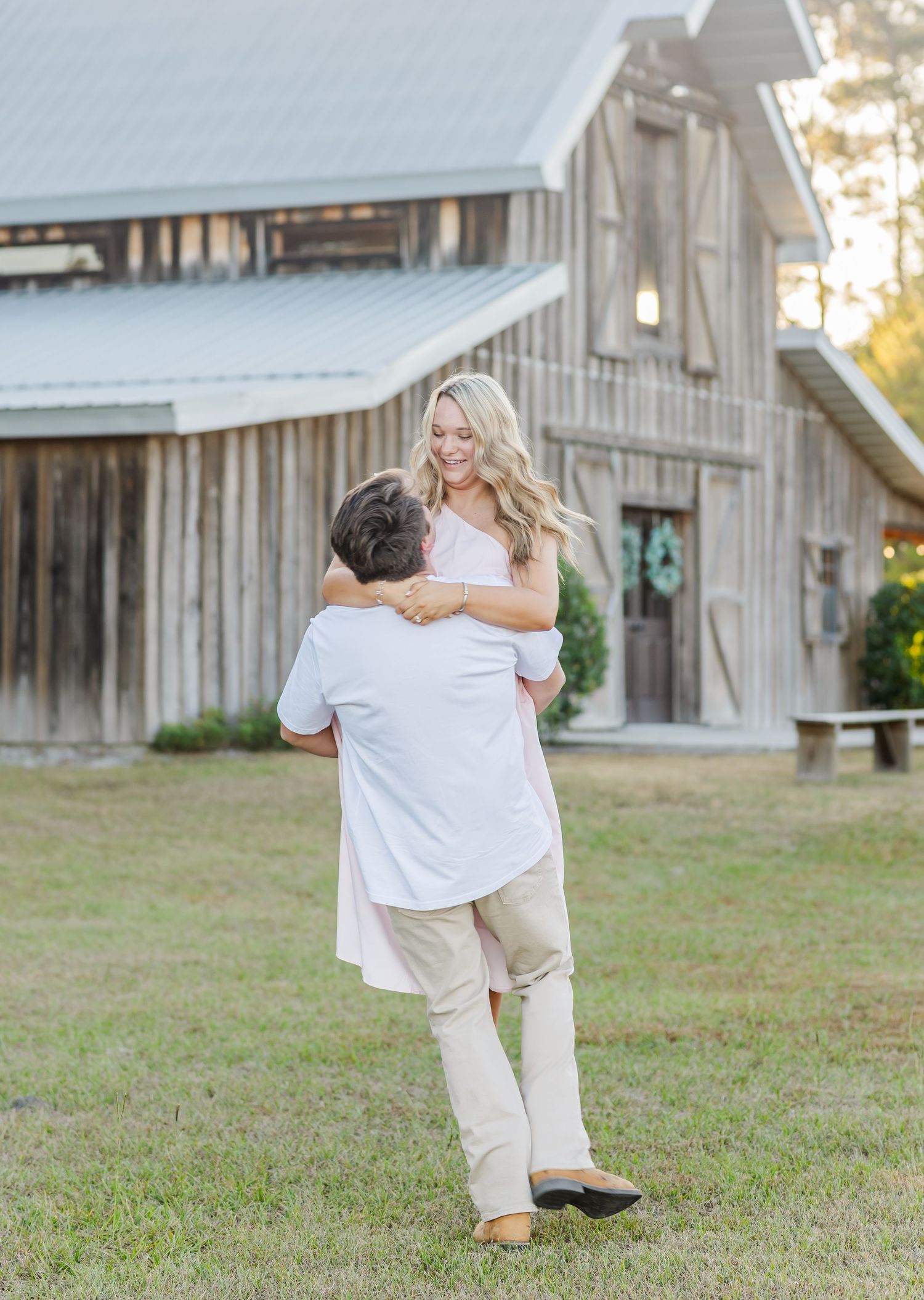 Joyful embrace in front of weathered barn during countryside engagement session.