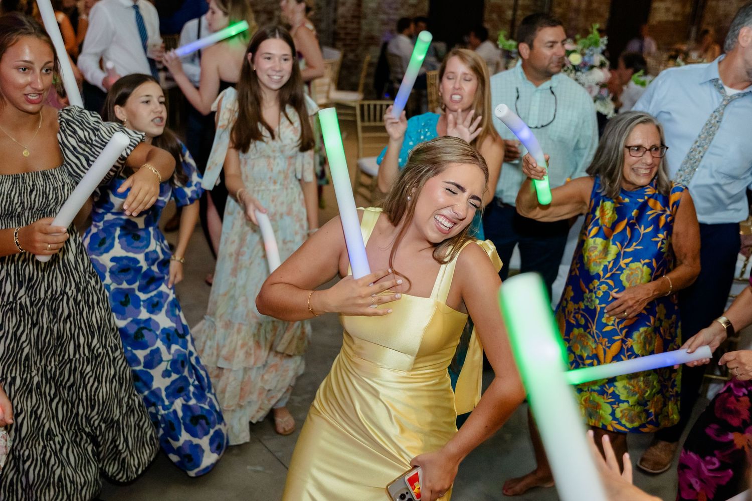 Crowd dances with colorful light-up foam sticks during an indoor party celebration.