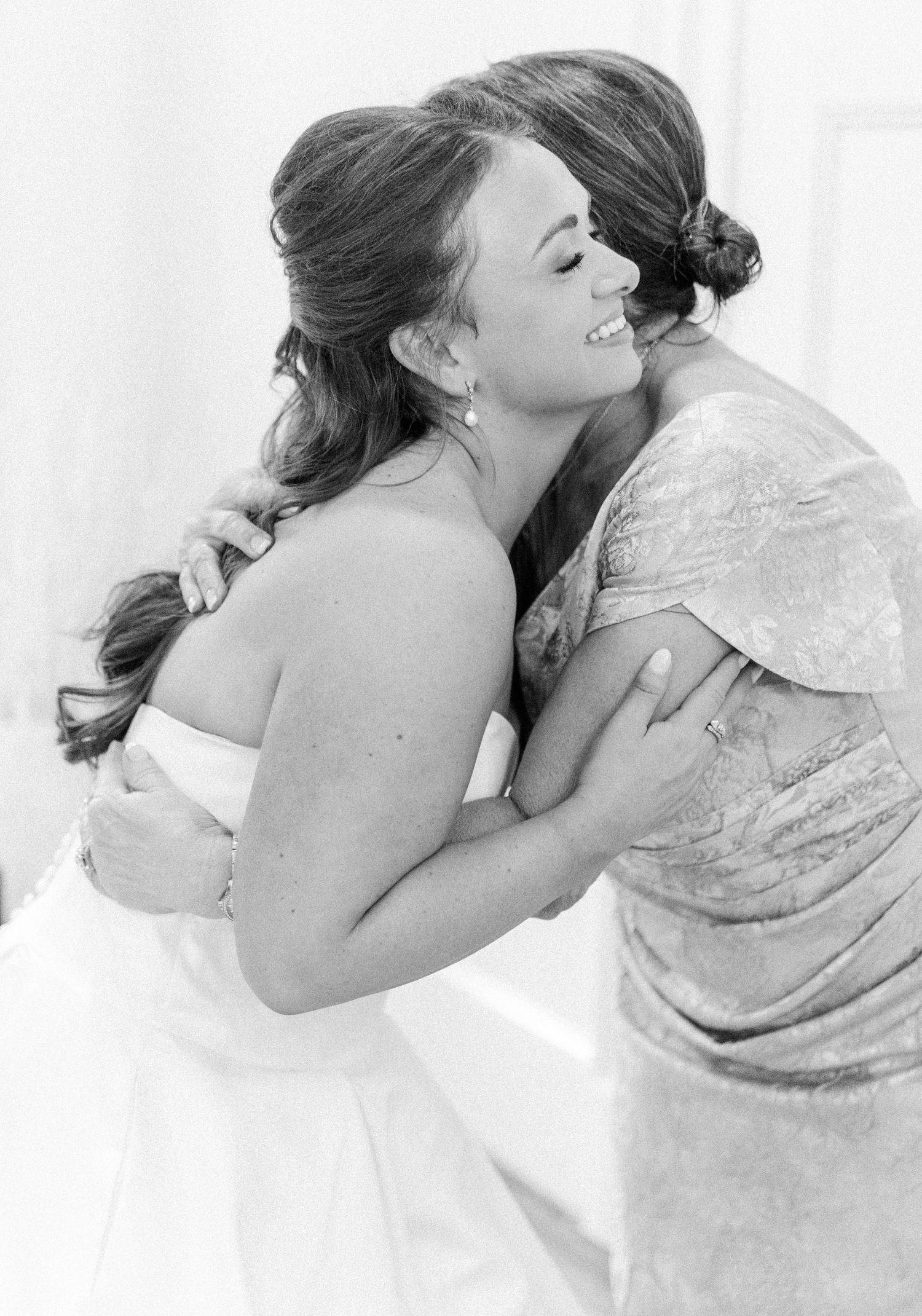 A tender black and white photograph captures an intimate embrace between two people in elegant attire.