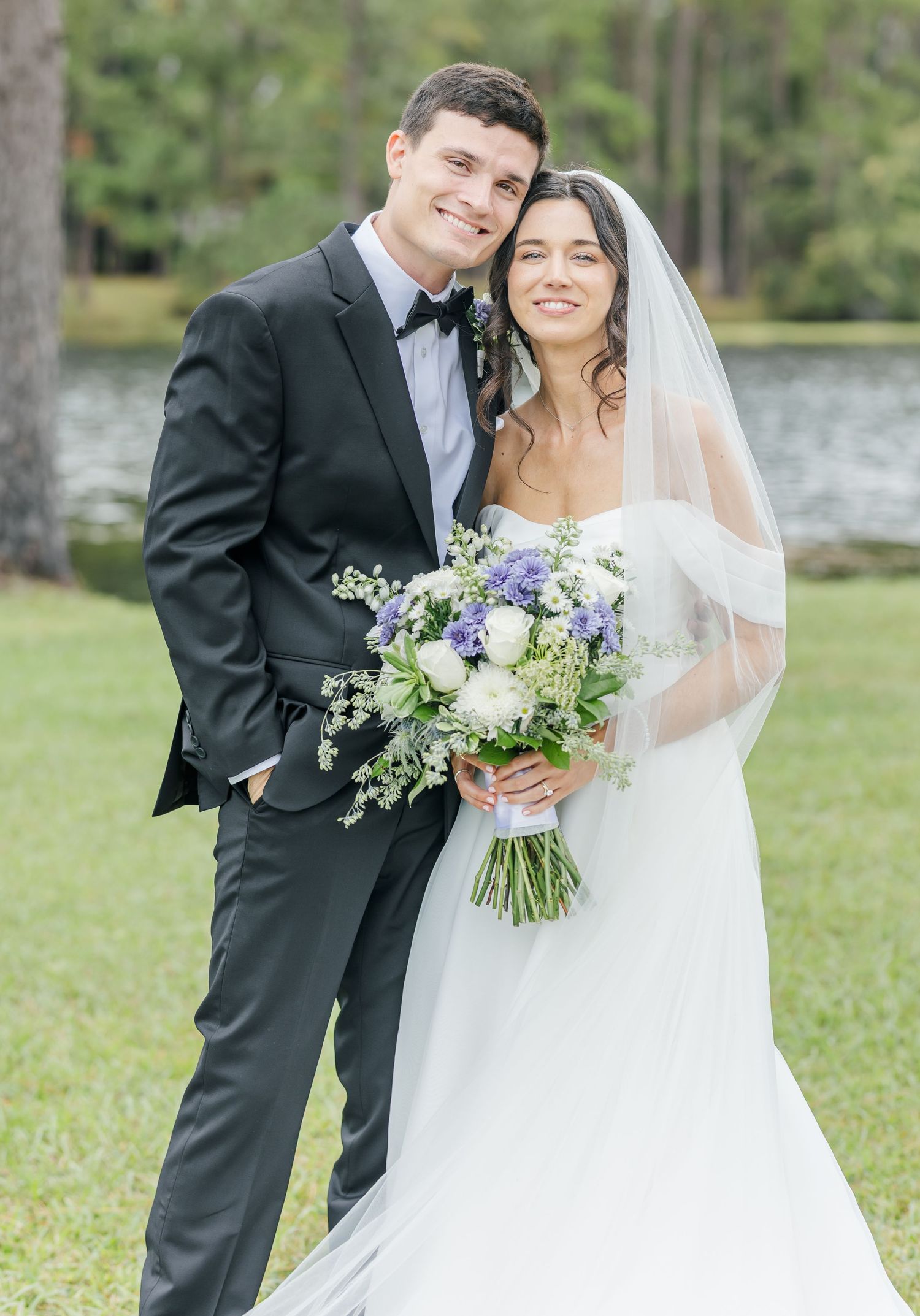 A romantic outdoor wedding photoshoot featuring a couple in traditional attire with purple and white floral bouquet.