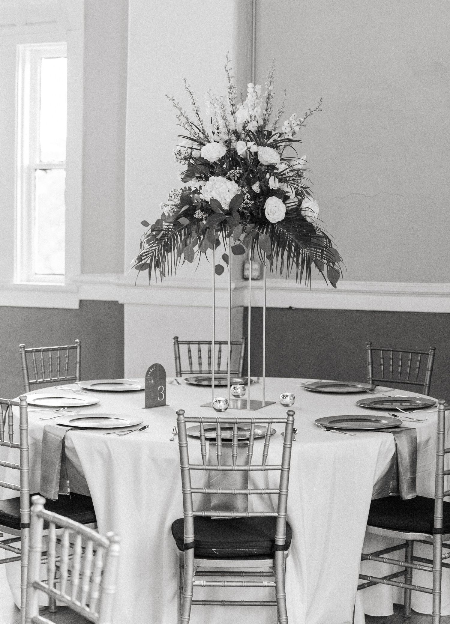 Elegant wedding reception venue with white linens and silver chiavari chairs set for formal dining.