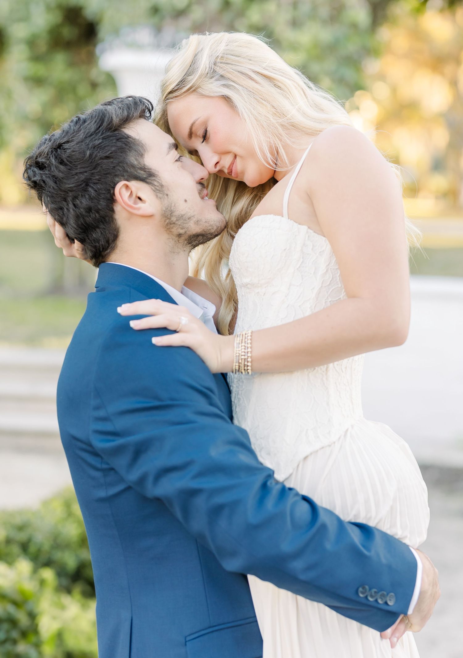 A couple in wedding attire share an intimate moment outdoors in a romantic garden setting.