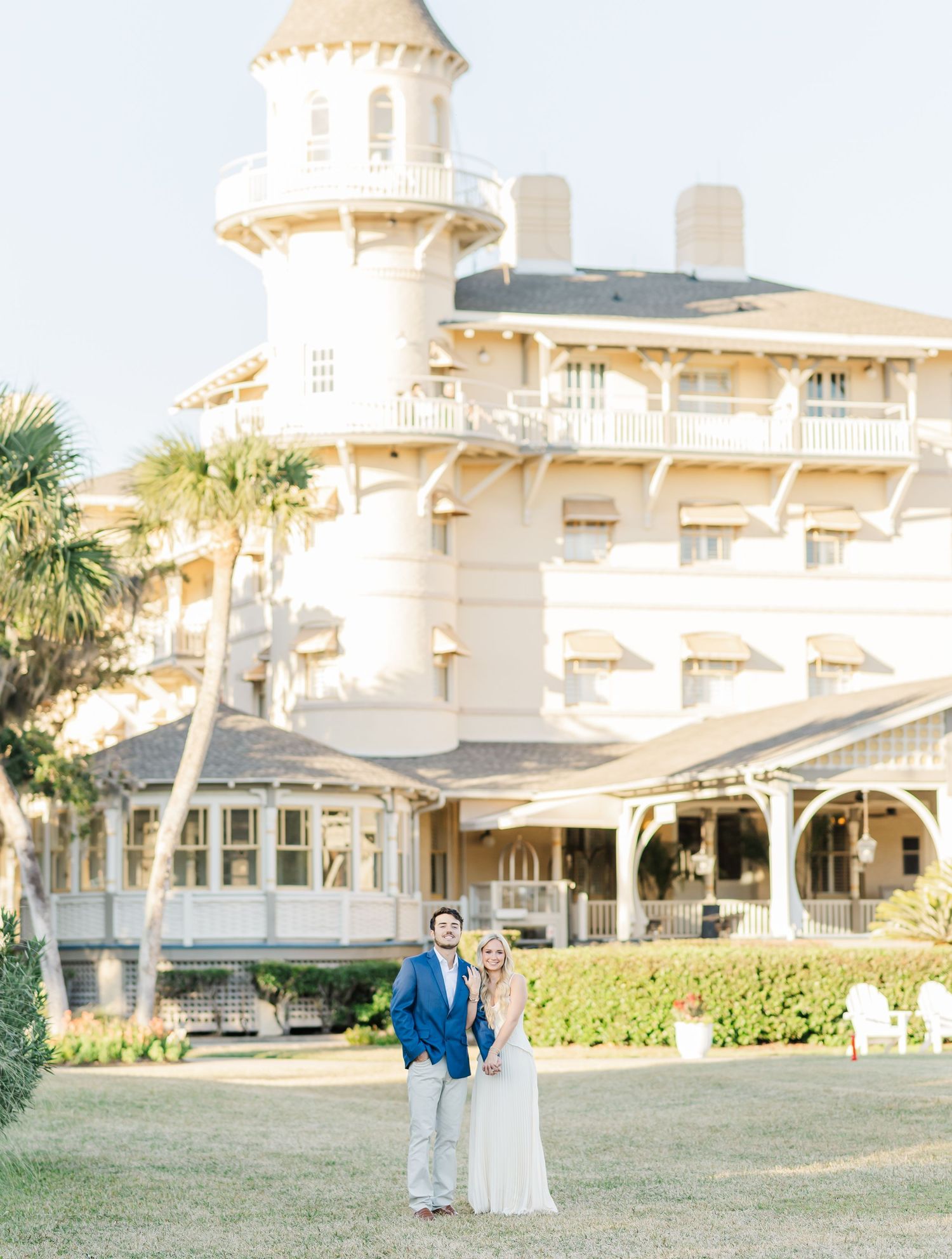 Elegant white Victorian-style mansion with ornate architectural details serves as a picturesque wedding venue in a sunny setting.