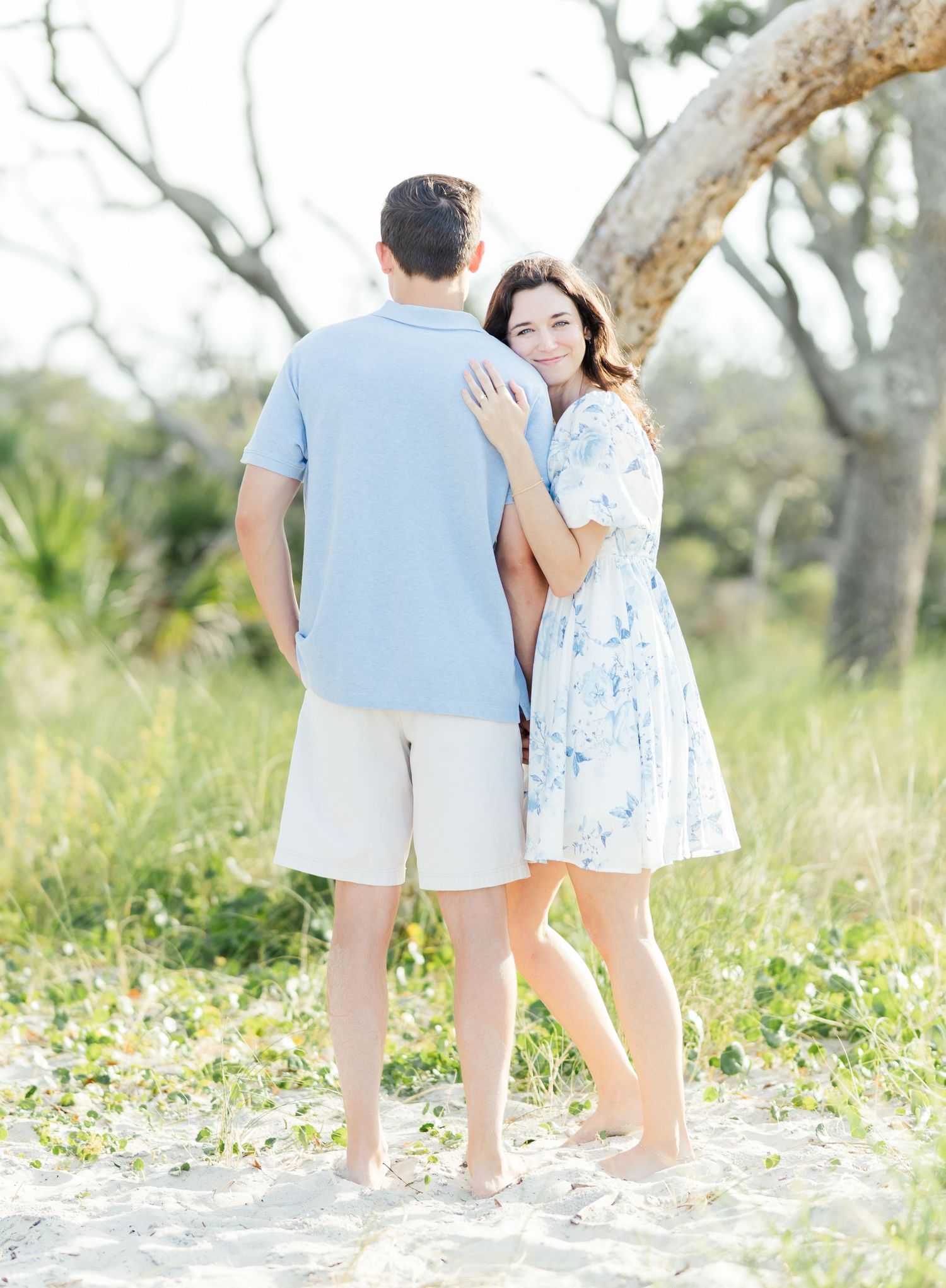 Couple in matching blue and white outfits walking together on sunny beach with driftwood.