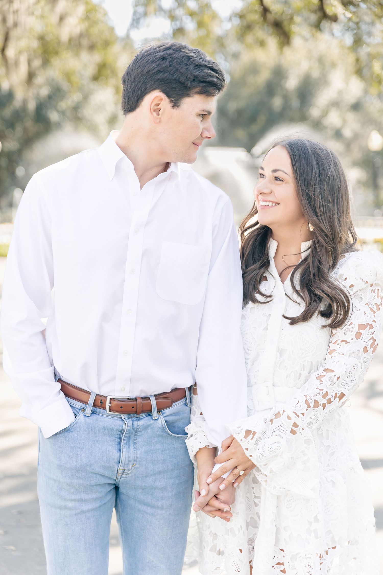 A couple in casual white and denim outfits share tender moments while posing together in a sunlit outdoor setting.