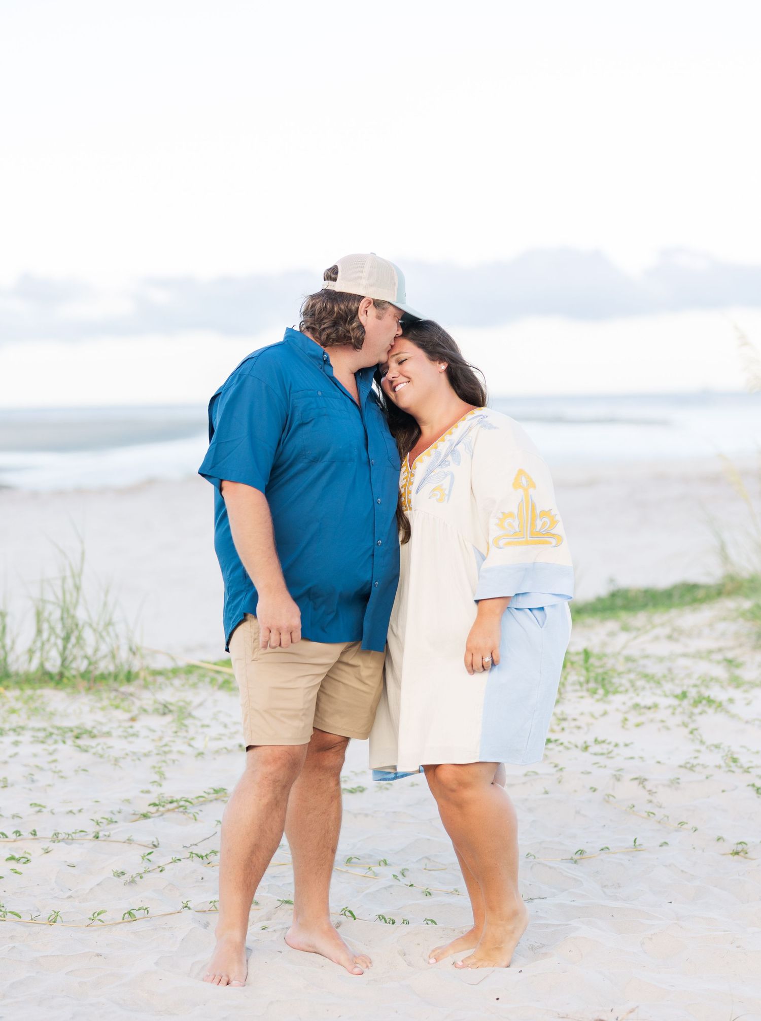 A couple sharing an intimate moment on the beach wearing casual summer attire.