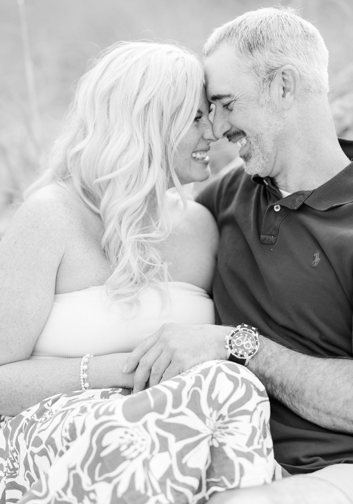 An affectionate couple in casual attire lean in close together for a monochrome portrait photo.