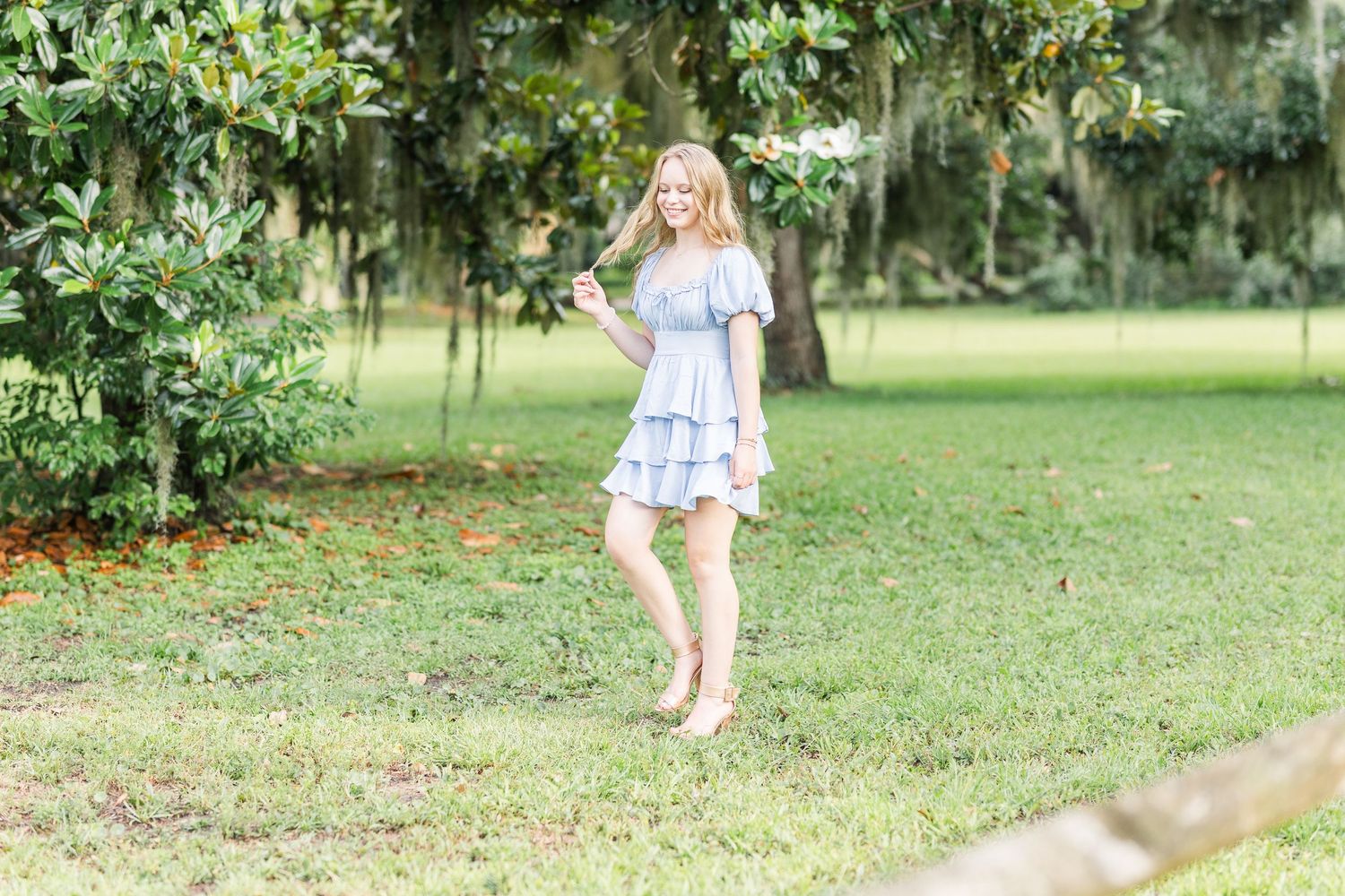 Garden photoshoot featuring a light blue tiered dress against mossy oak trees and green landscaping.