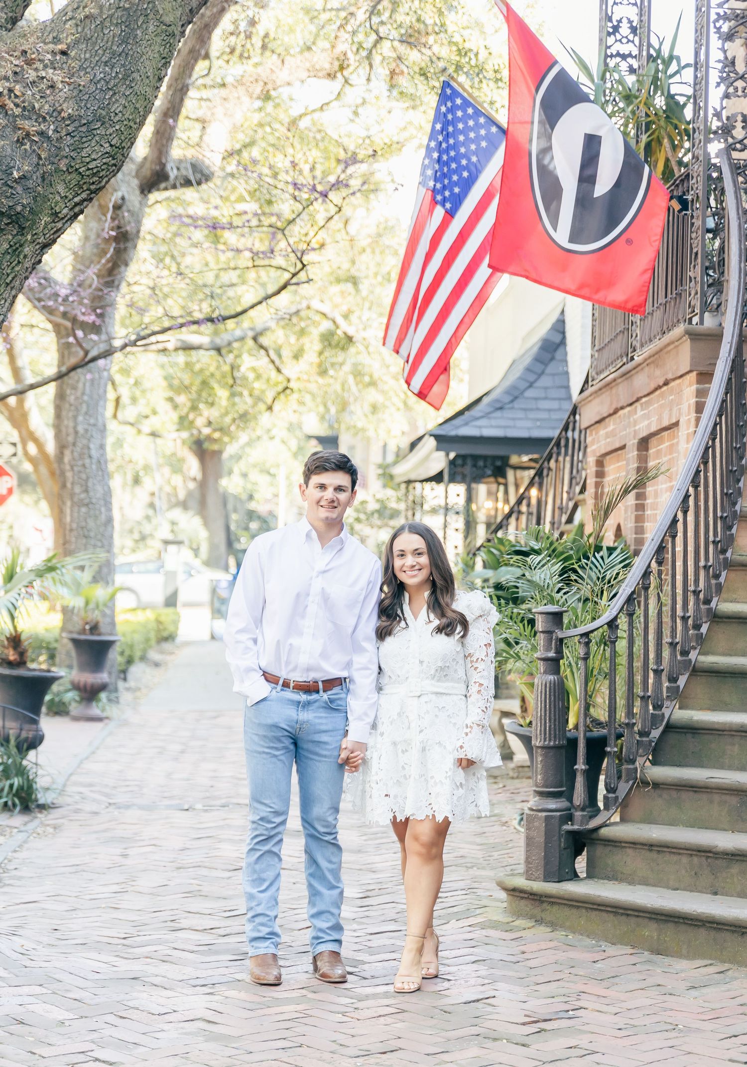 Engaged couple standing on brick pathway with American and state flags displayed above.