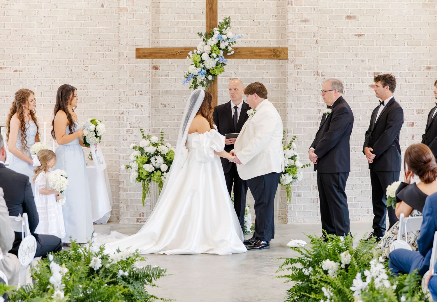 Wedding ceremony at the altar with bride and groom exchanging vows beneath a floral cross.