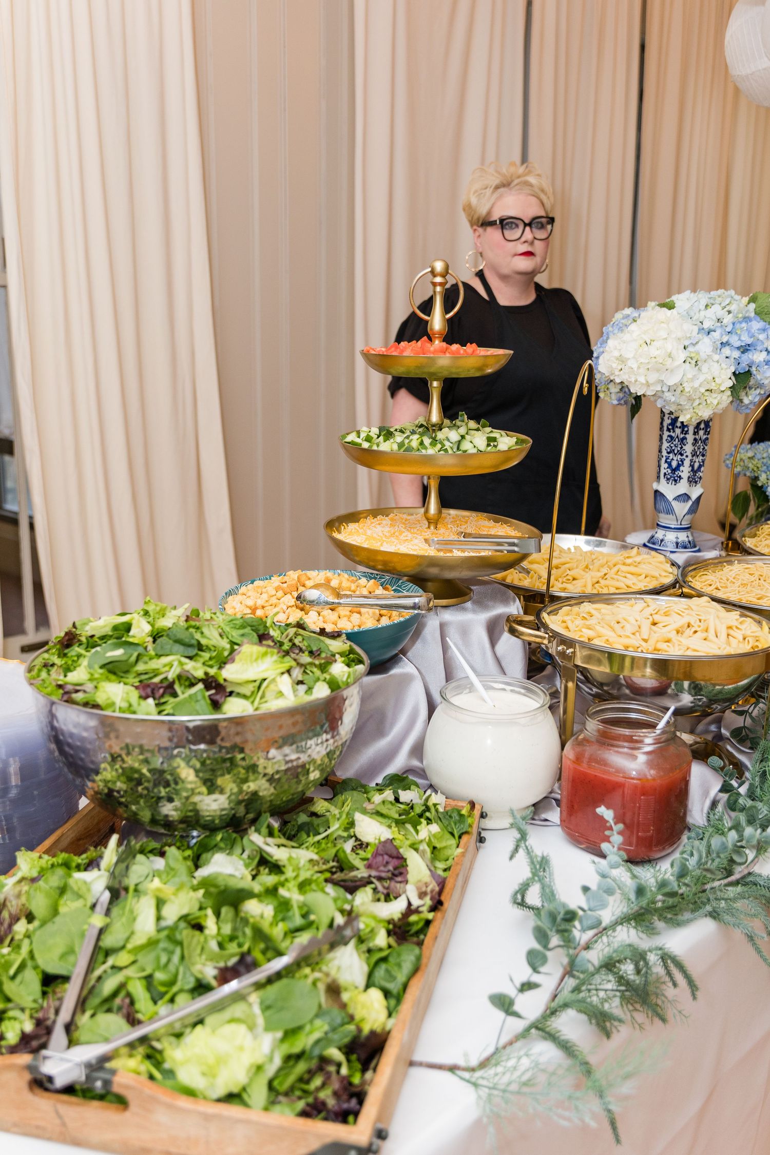 Elegant wedding reception buffet spread with fresh salads, pasta dishes, and tiered gold serving stand.