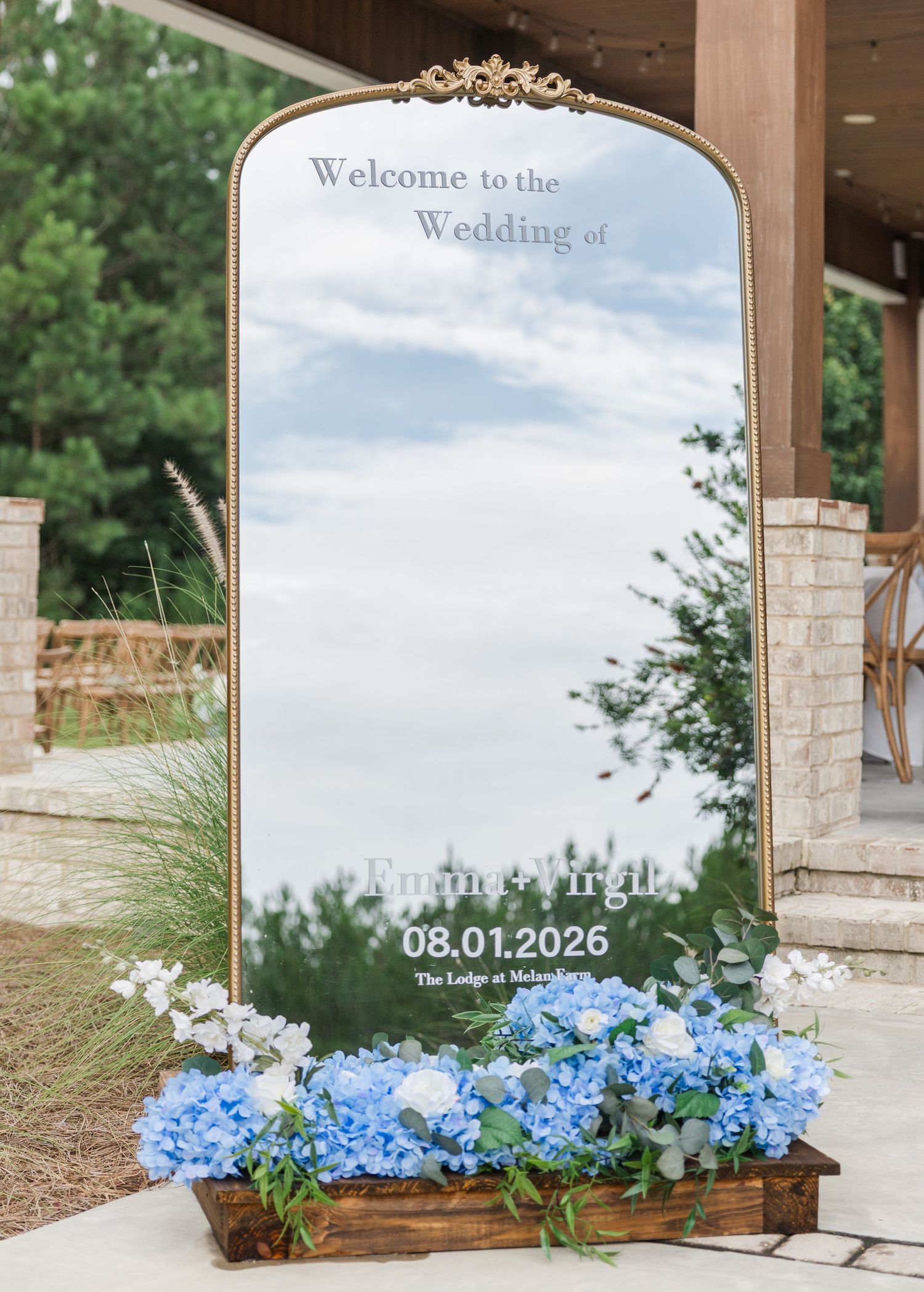 Elegant gold-framed wedding welcome mirror sign with blue hydrangeas, displaying wedding date 08.01.2026 at The Lodge at Malvern.