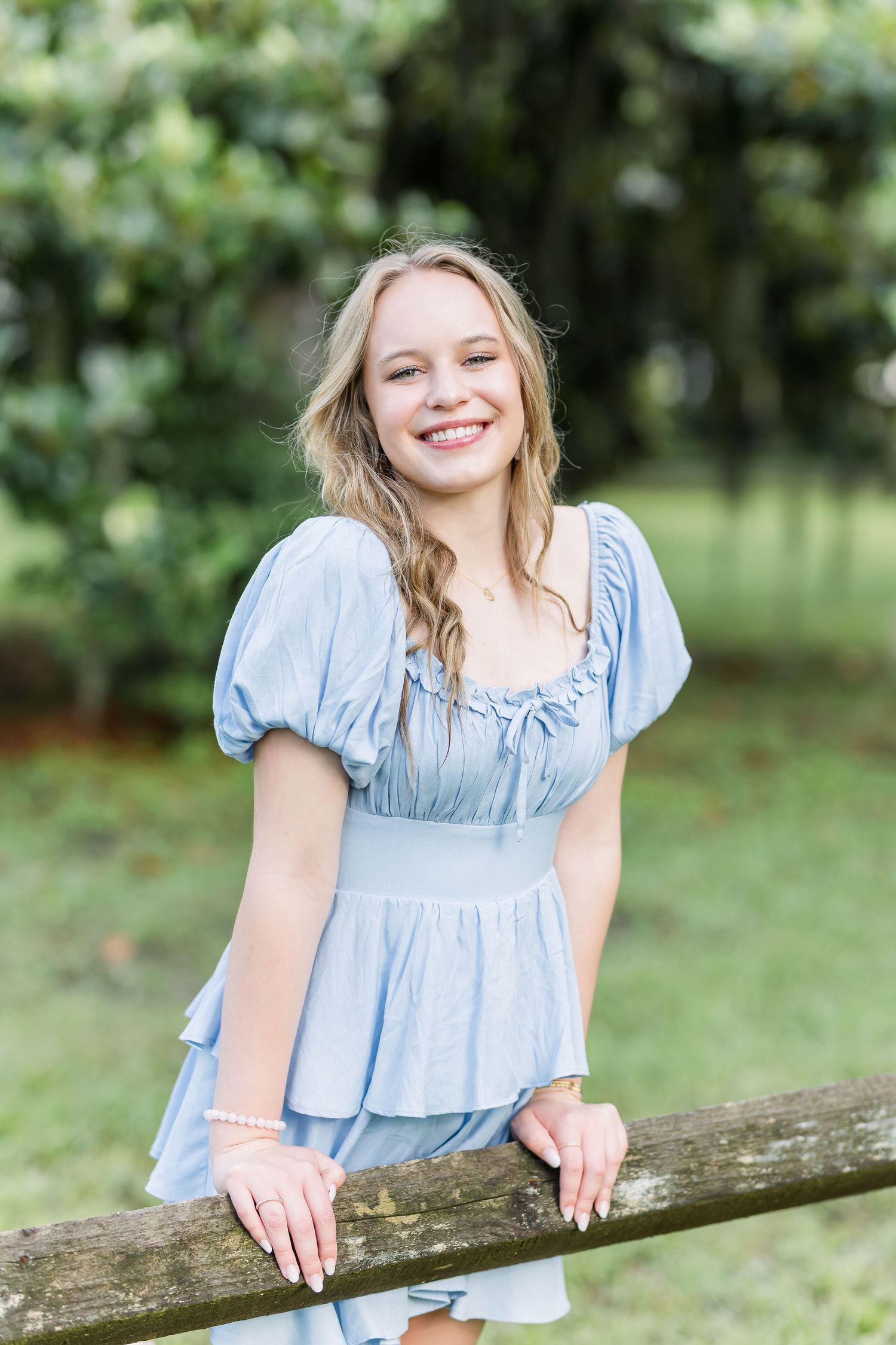 Natural outdoor portrait session featuring a light blue ruffle top and wooden fence backdrop.