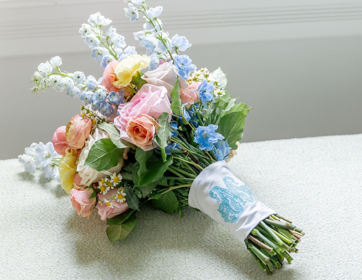 Delicate spring wedding bouquet featuring pink roses, blue flowers, and green foliage.
