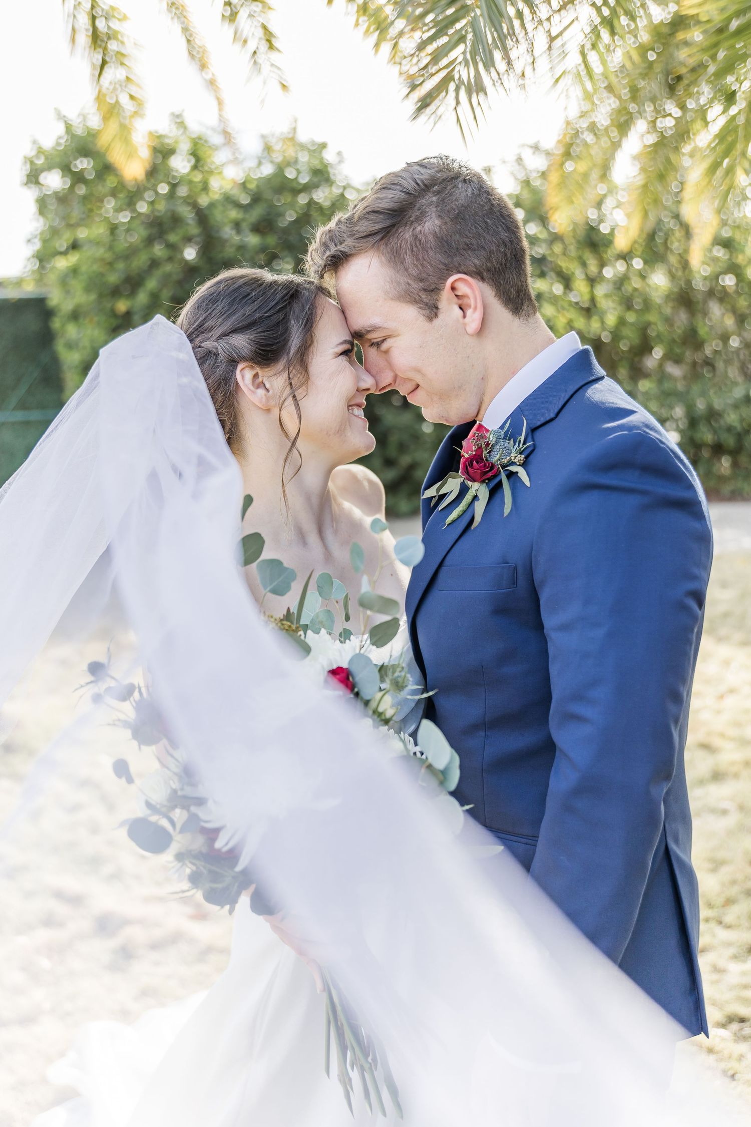 Romantic wedding portrait with couple beneath palm trees and natural lighting.