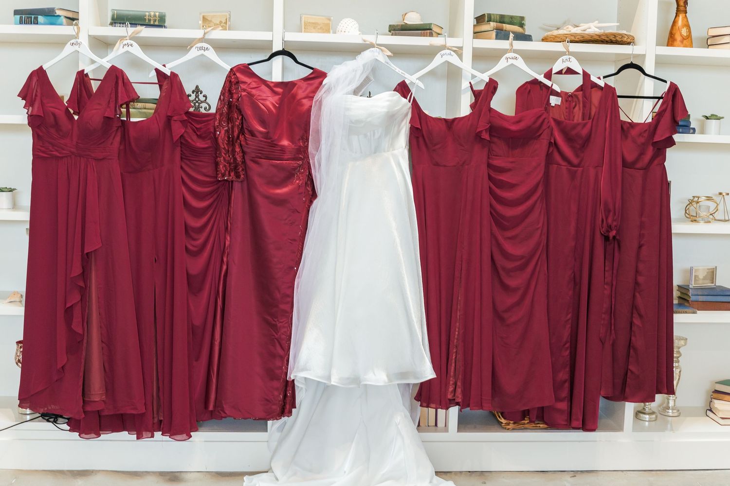 Bridal party dresses displayed on hangers showing white wedding gown centered among burgundy bridesmaid dresses.