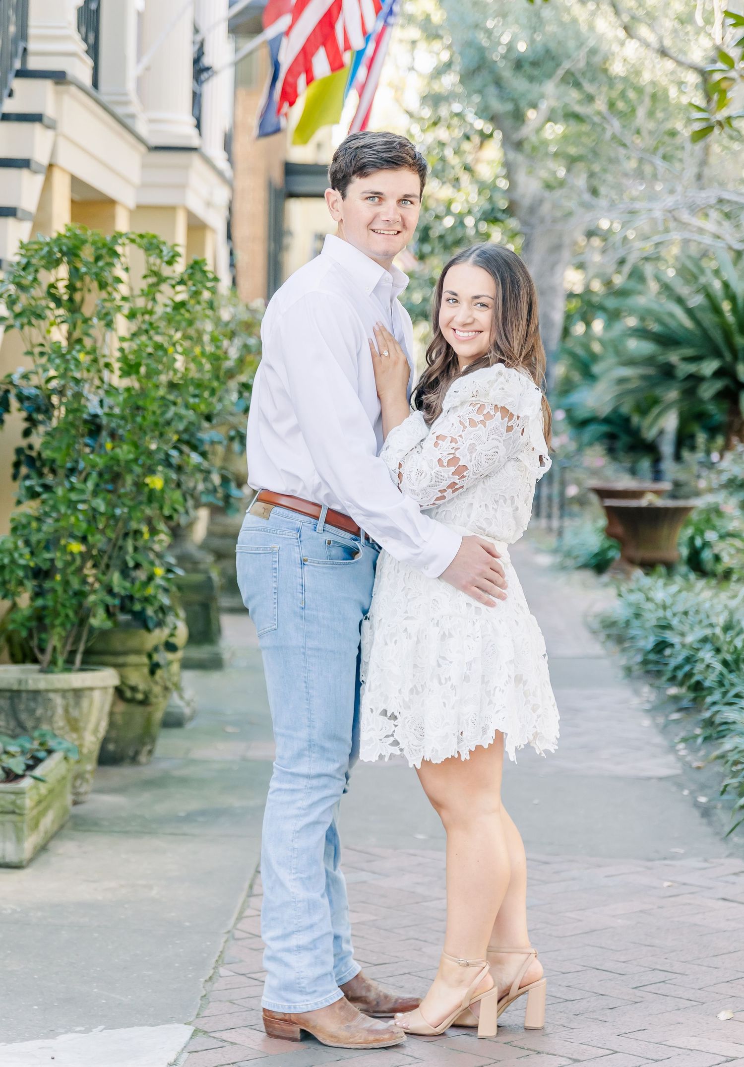 A romantic couple in white and denim embrace during a charming outdoor photoshoot on a stone path with greenery surroundings.