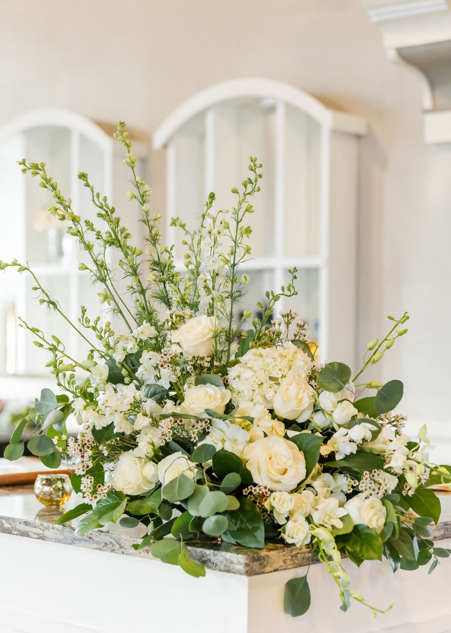 Lush white rose and eucalyptus floral arrangement with delicate branches on marble surface at wedding venue.
