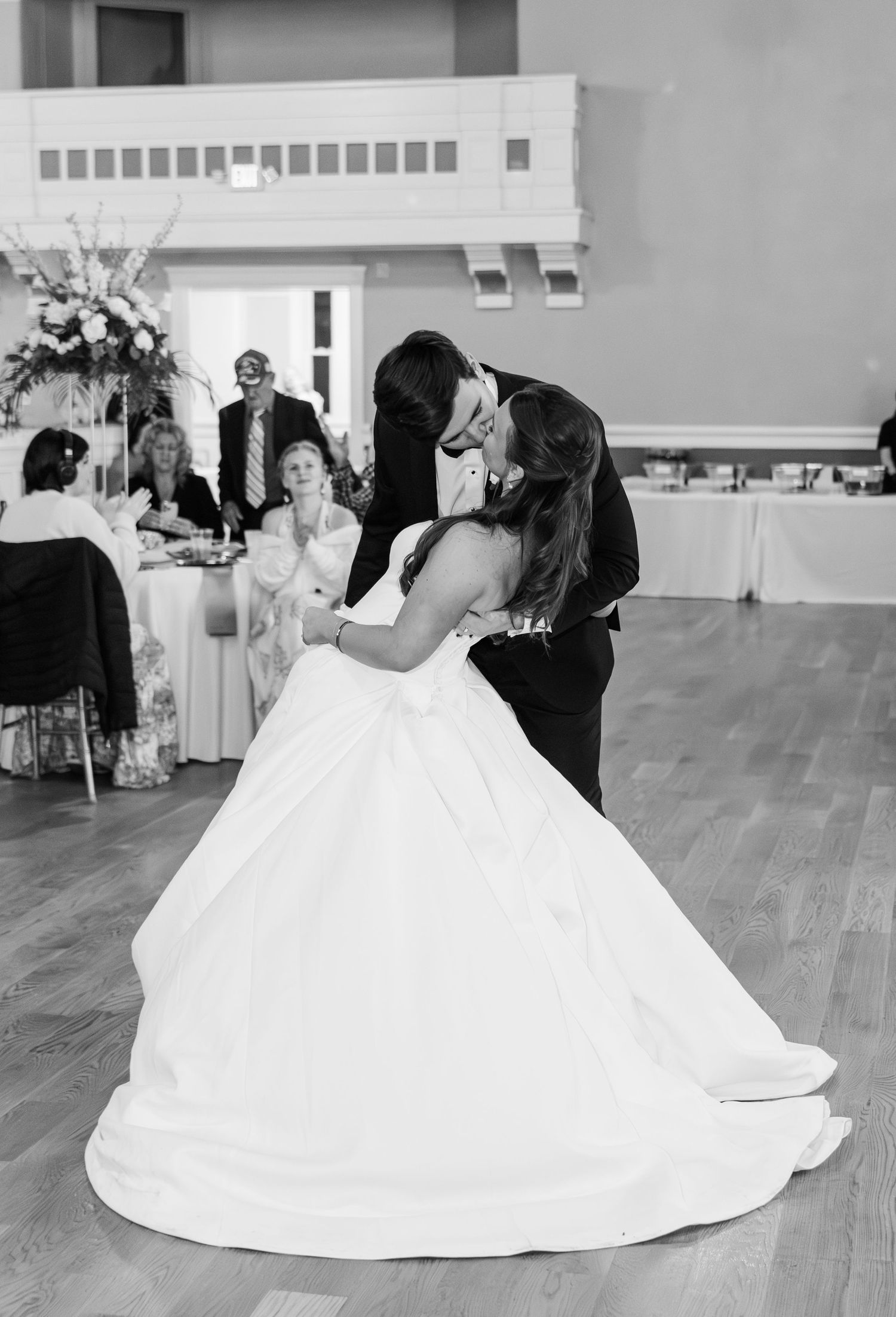 Bride and groom share a romantic first dance kiss in black and white wedding reception photo.