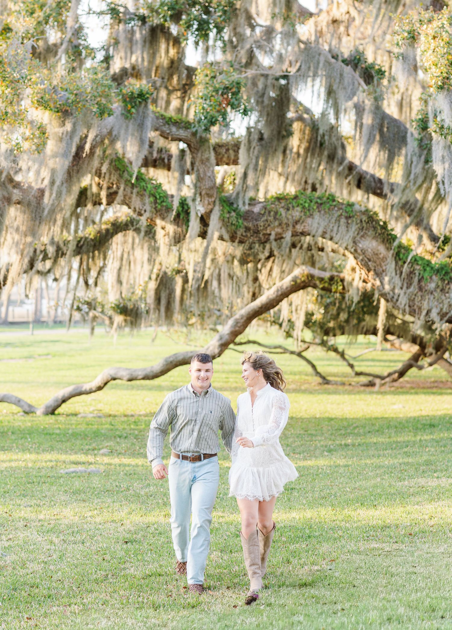 A couple dances playfully under Spanish moss draped oak trees in a sunlit Southern garden setting.