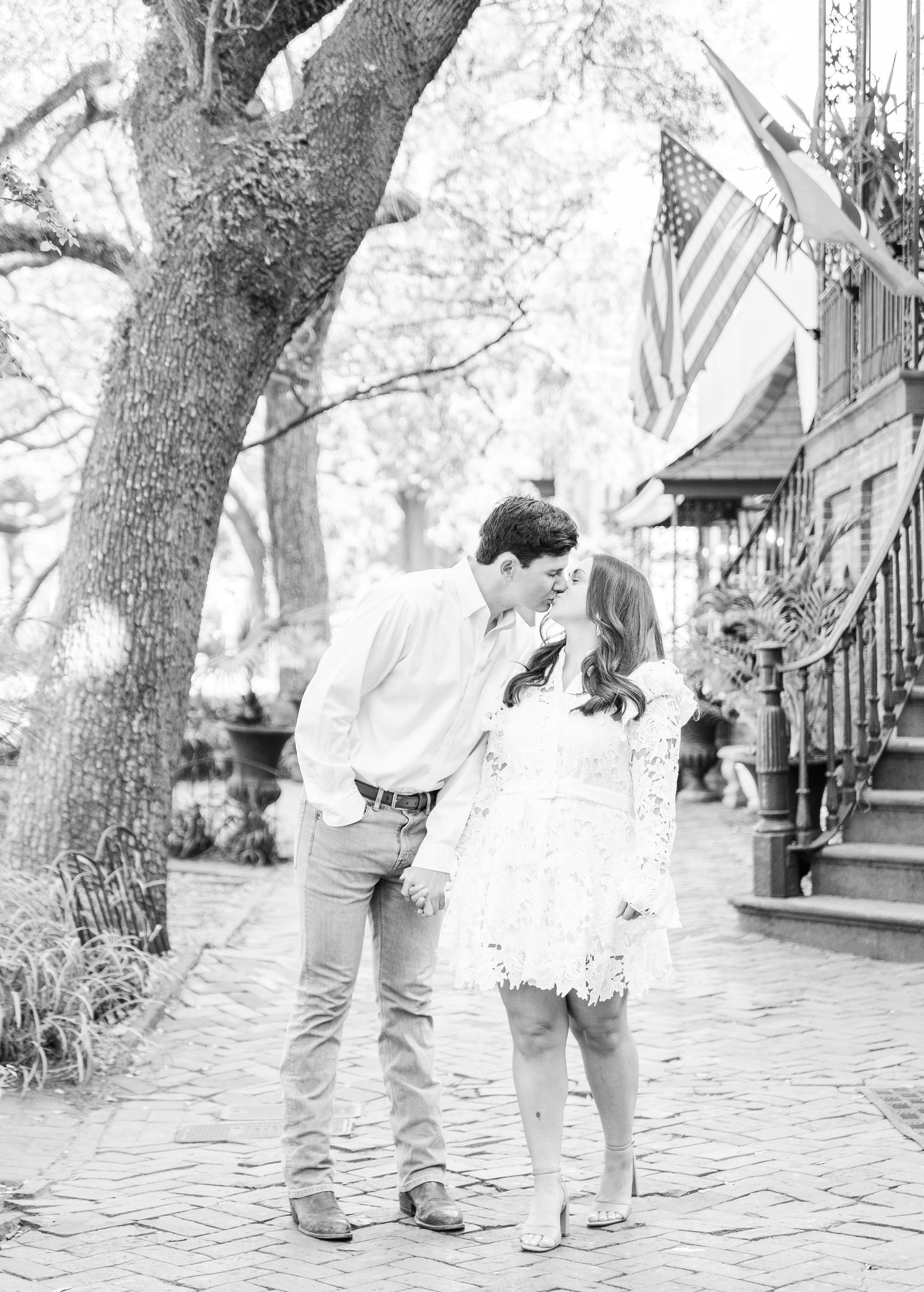 Black and white photo of a couple sharing a tender moment on a tree-lined street.