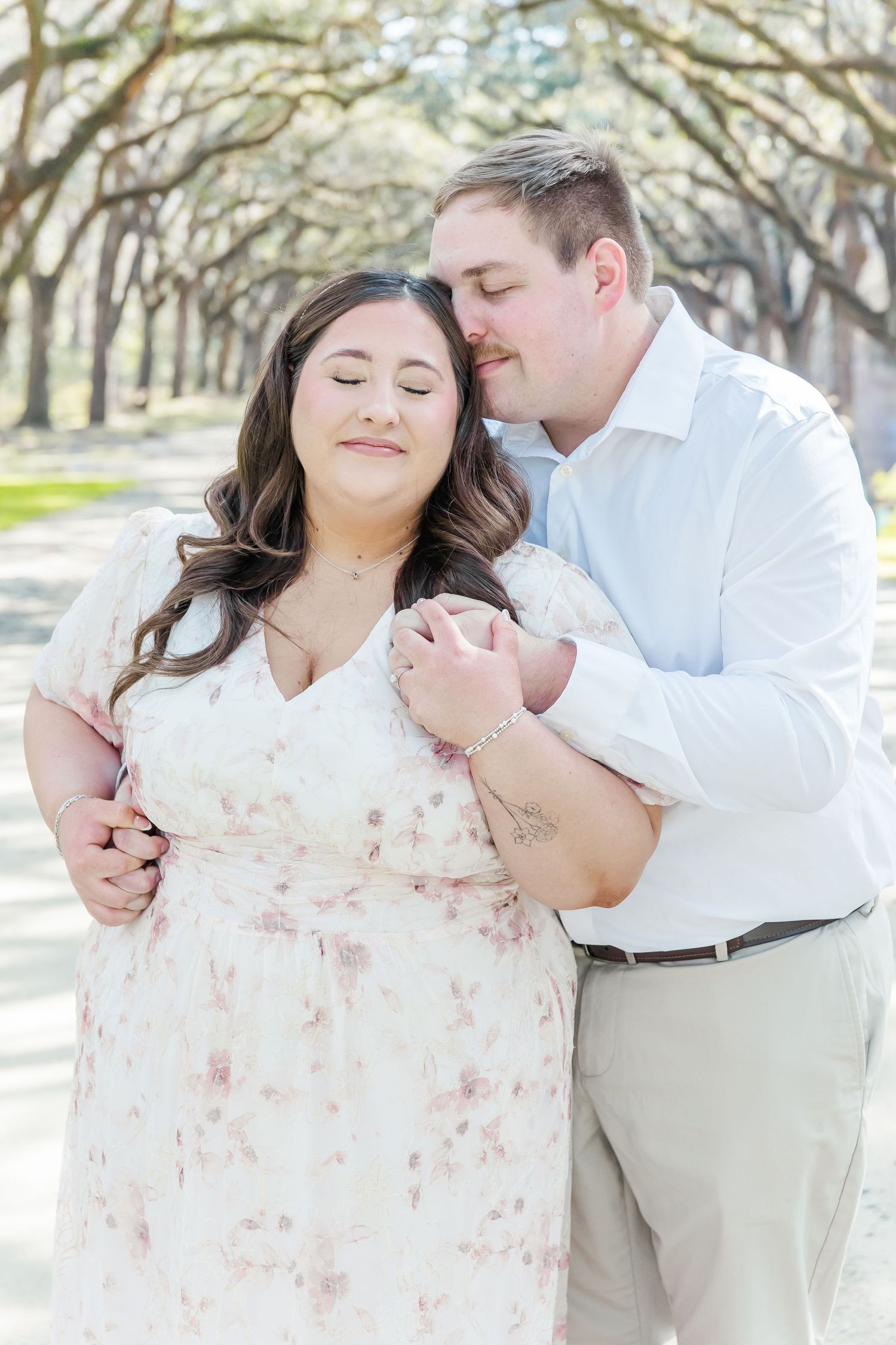 Tender moment between couple during spring engagement photos under oak trees.