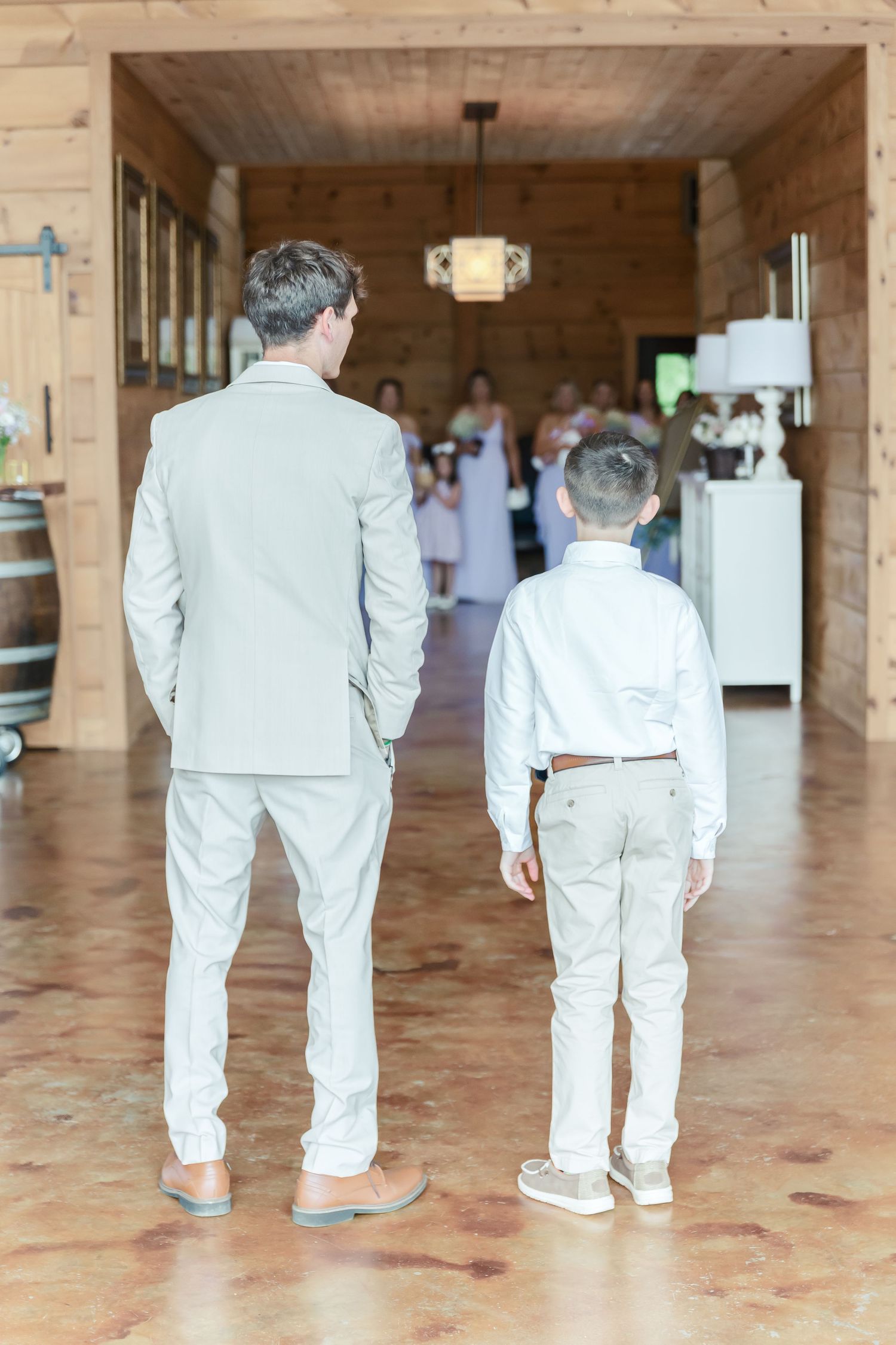 Two people in light-colored suits stand looking down a rustic wooden hallway.