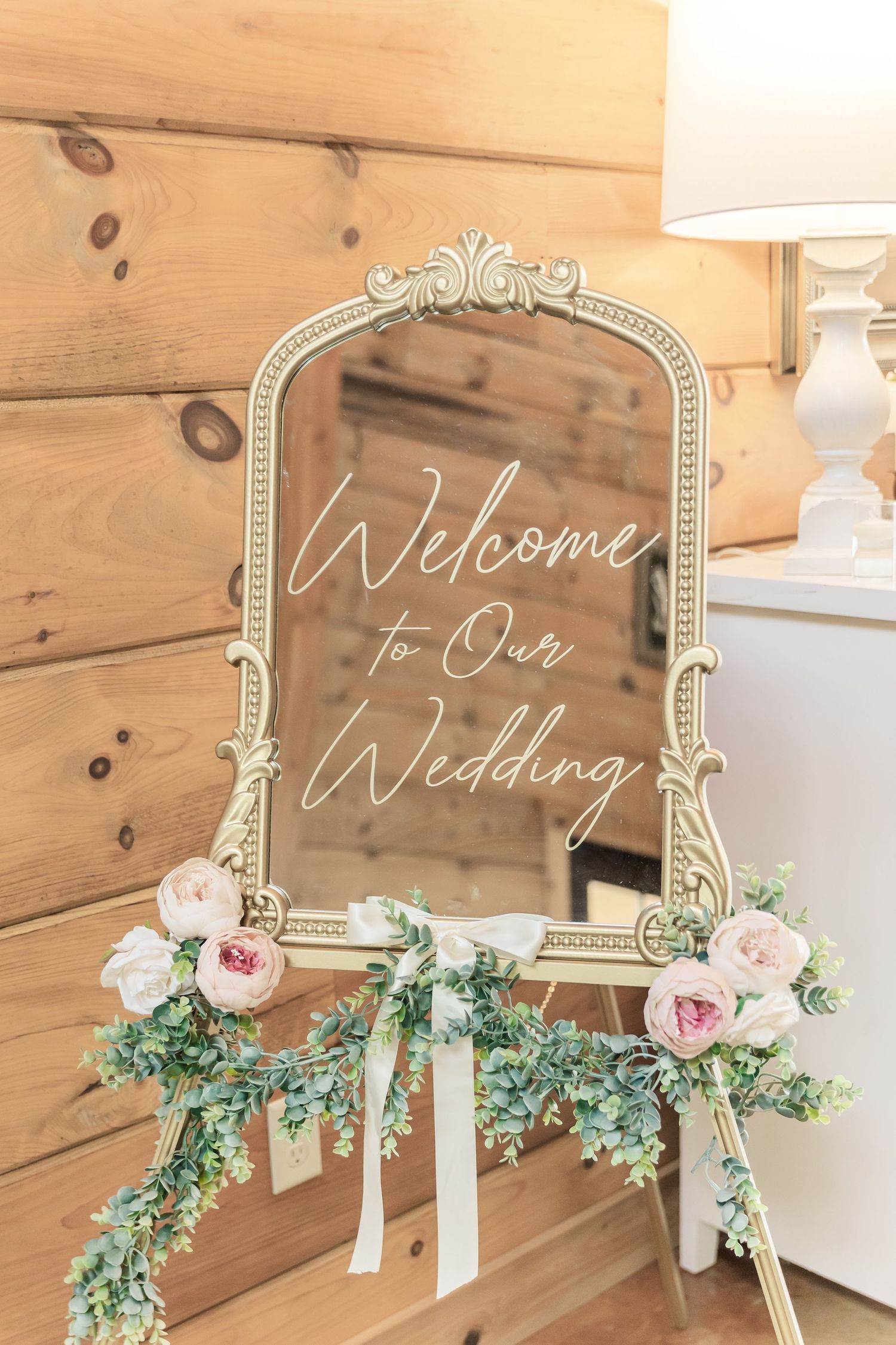 Ornate vintage mirror with 'Welcome to Our Wedding' text decorated with roses and greenery.