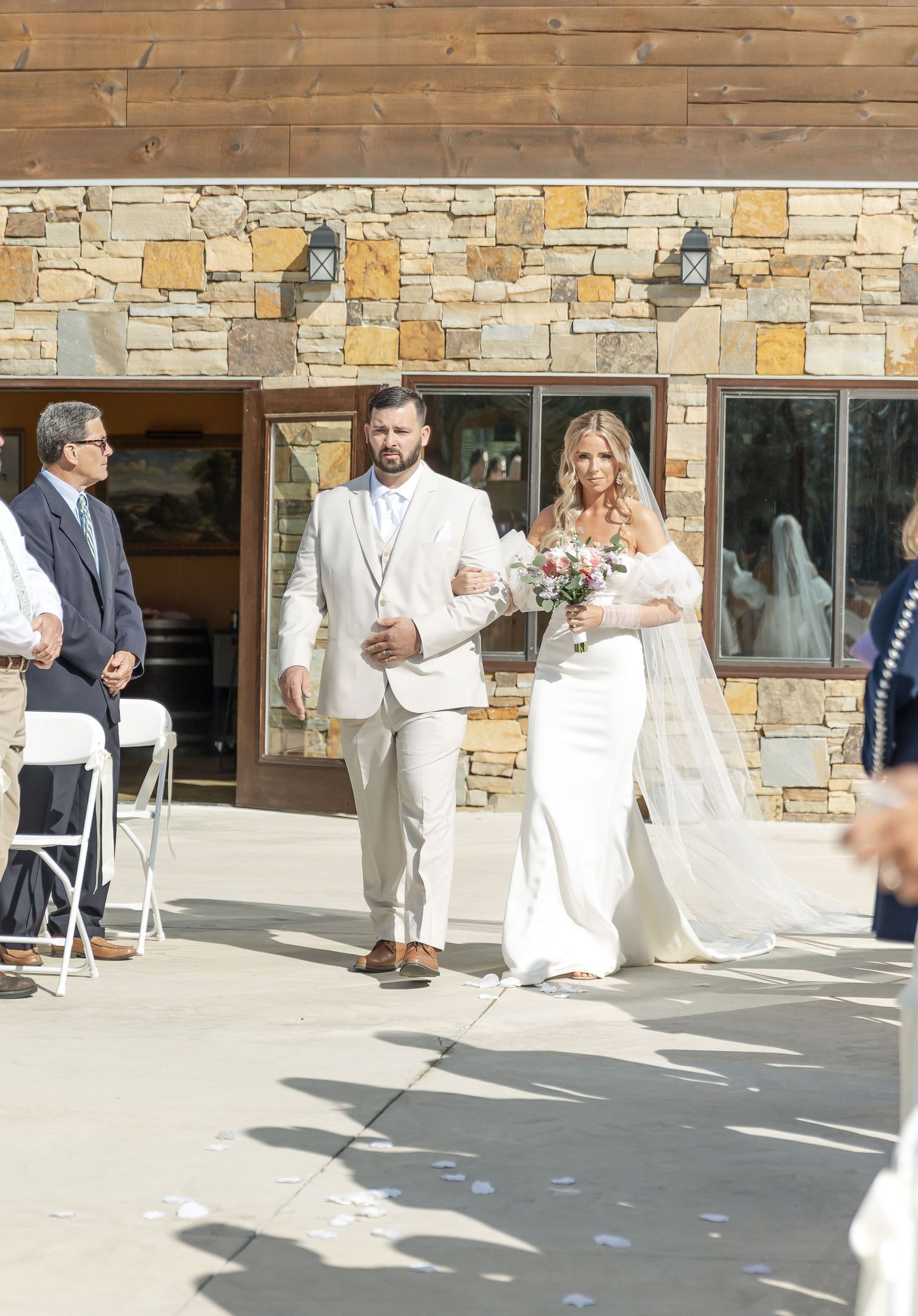 Wedding couple walking down aisle at venue with stone and wood architecture.