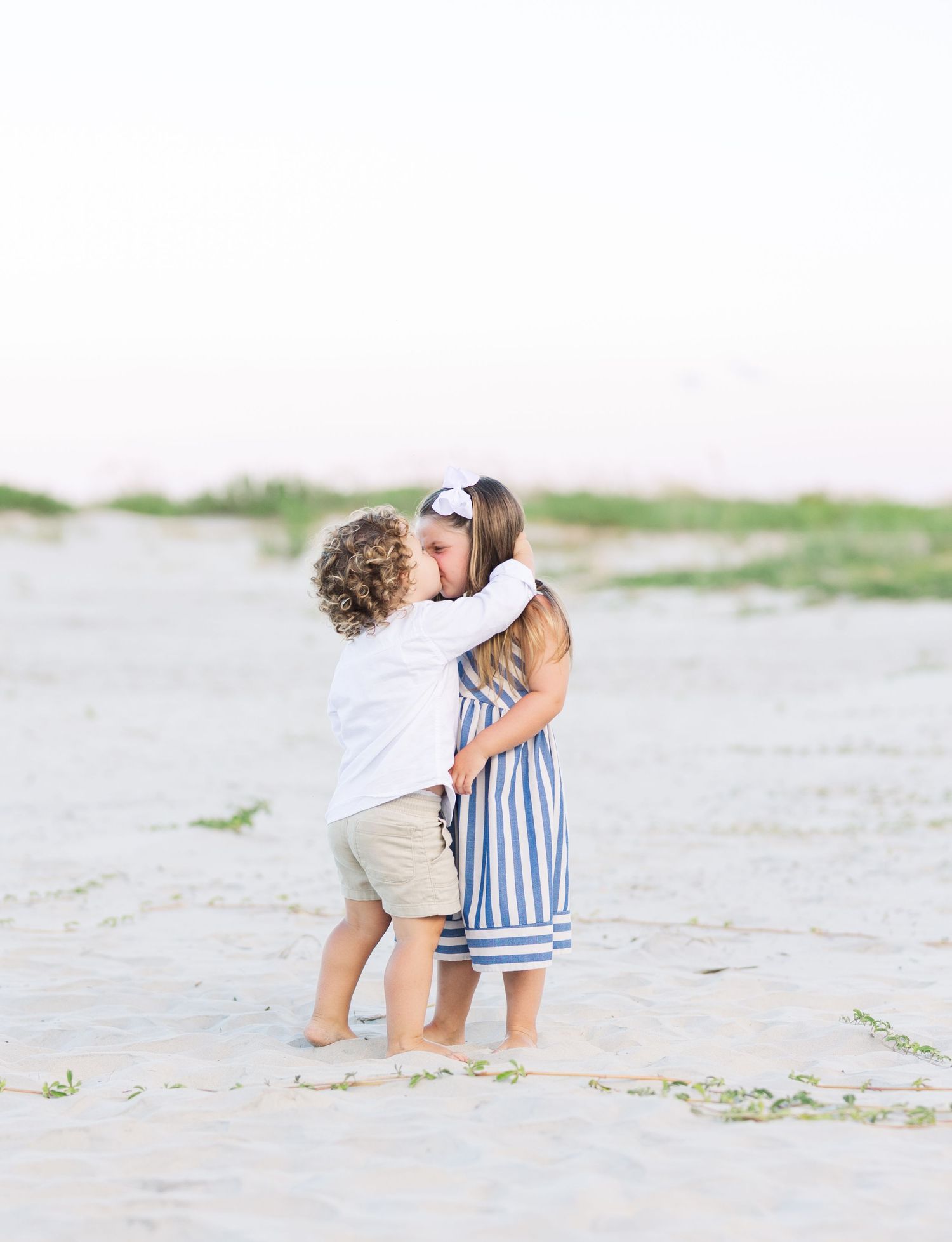 Two children embrace and dance together on a sandy beach.