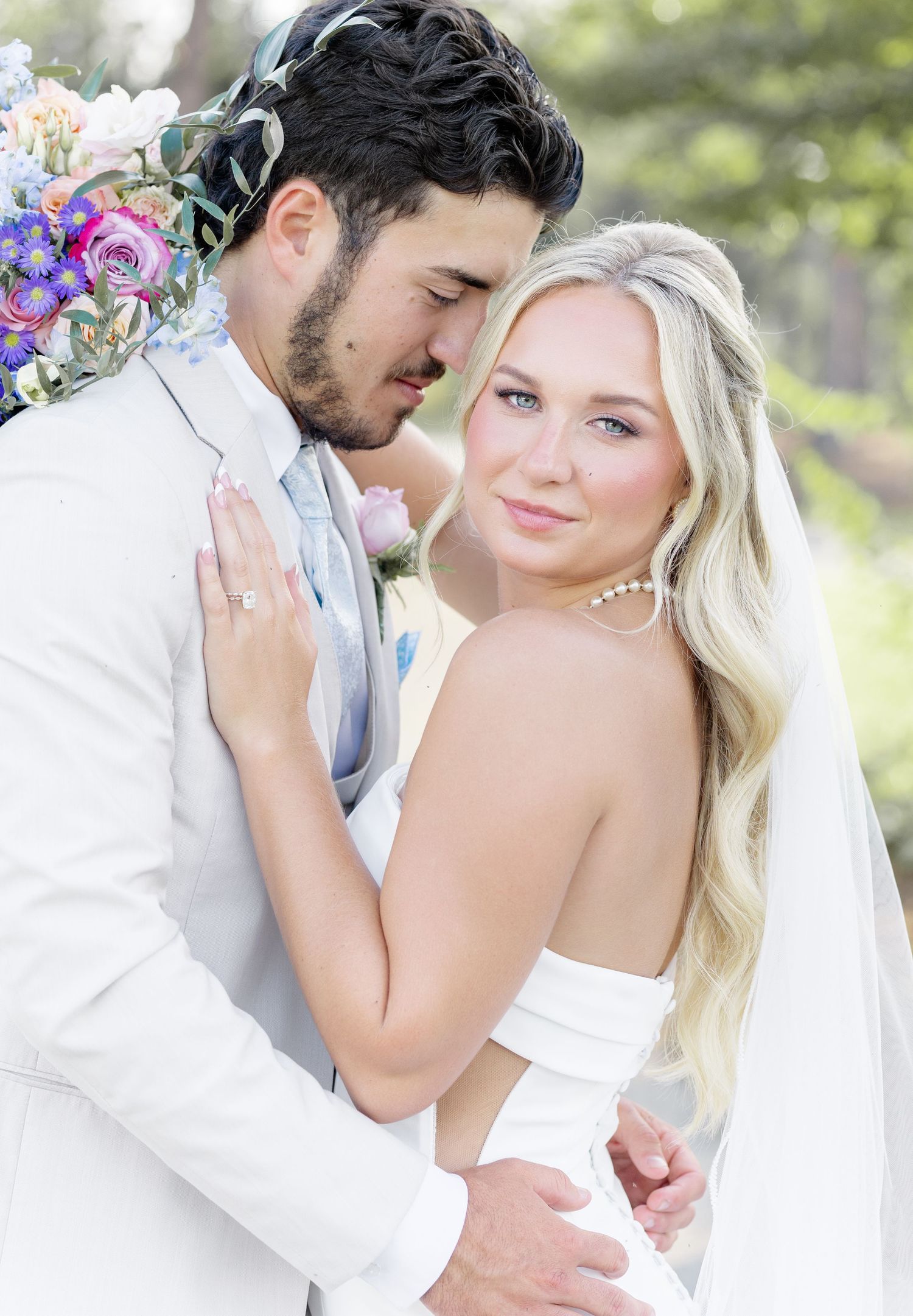 Bride and groom share an intimate romantic pose, she in a strapless gown with veil, he in a white suit.