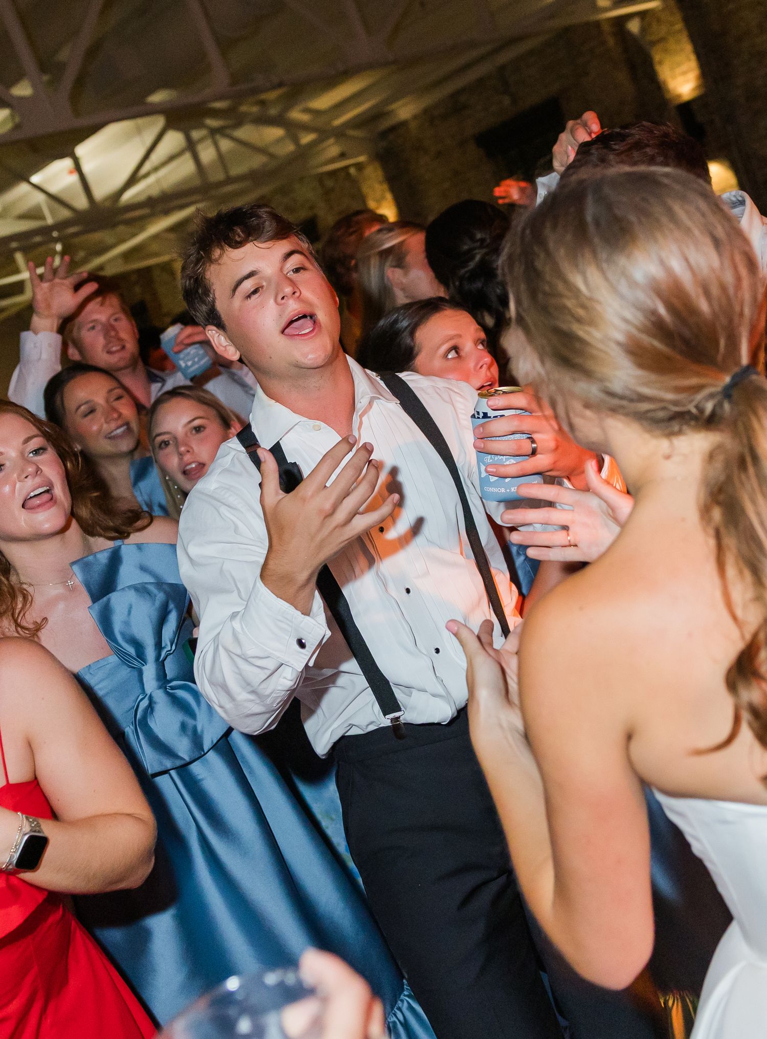 Energetic wedding guest in white shirt dancing enthusiastically with crowd at lively wedding reception party.