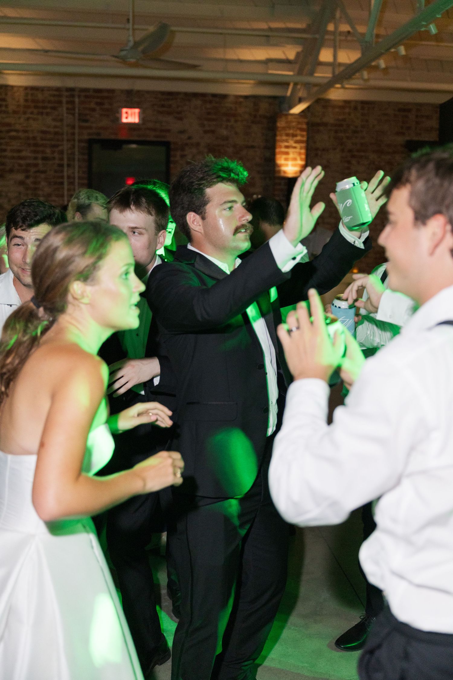 Bride and guests dancing under green lights at lively wedding reception celebration.
