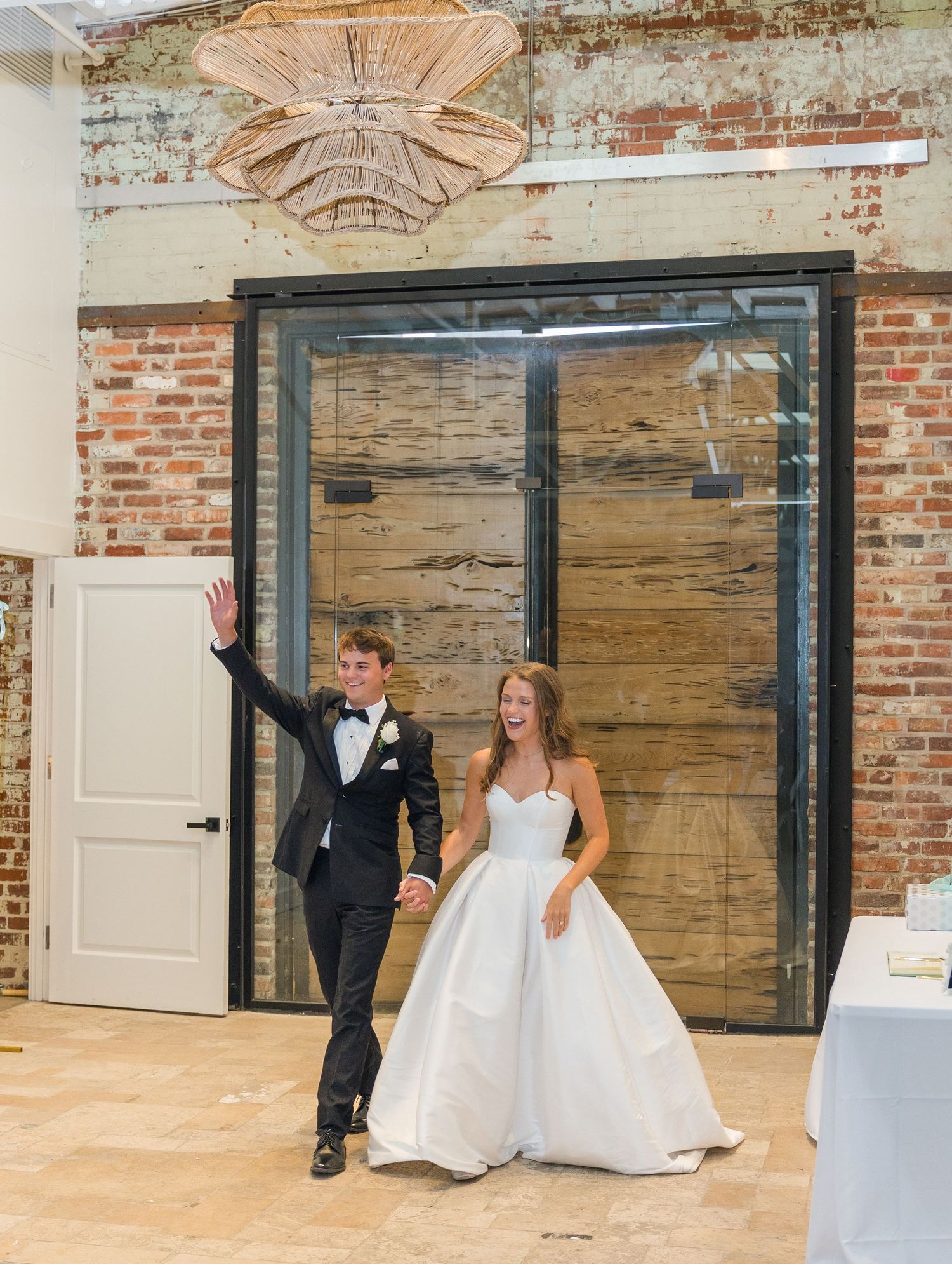 Newlyweds make grand reception entrance through large wooden doors as groom waves to guests.