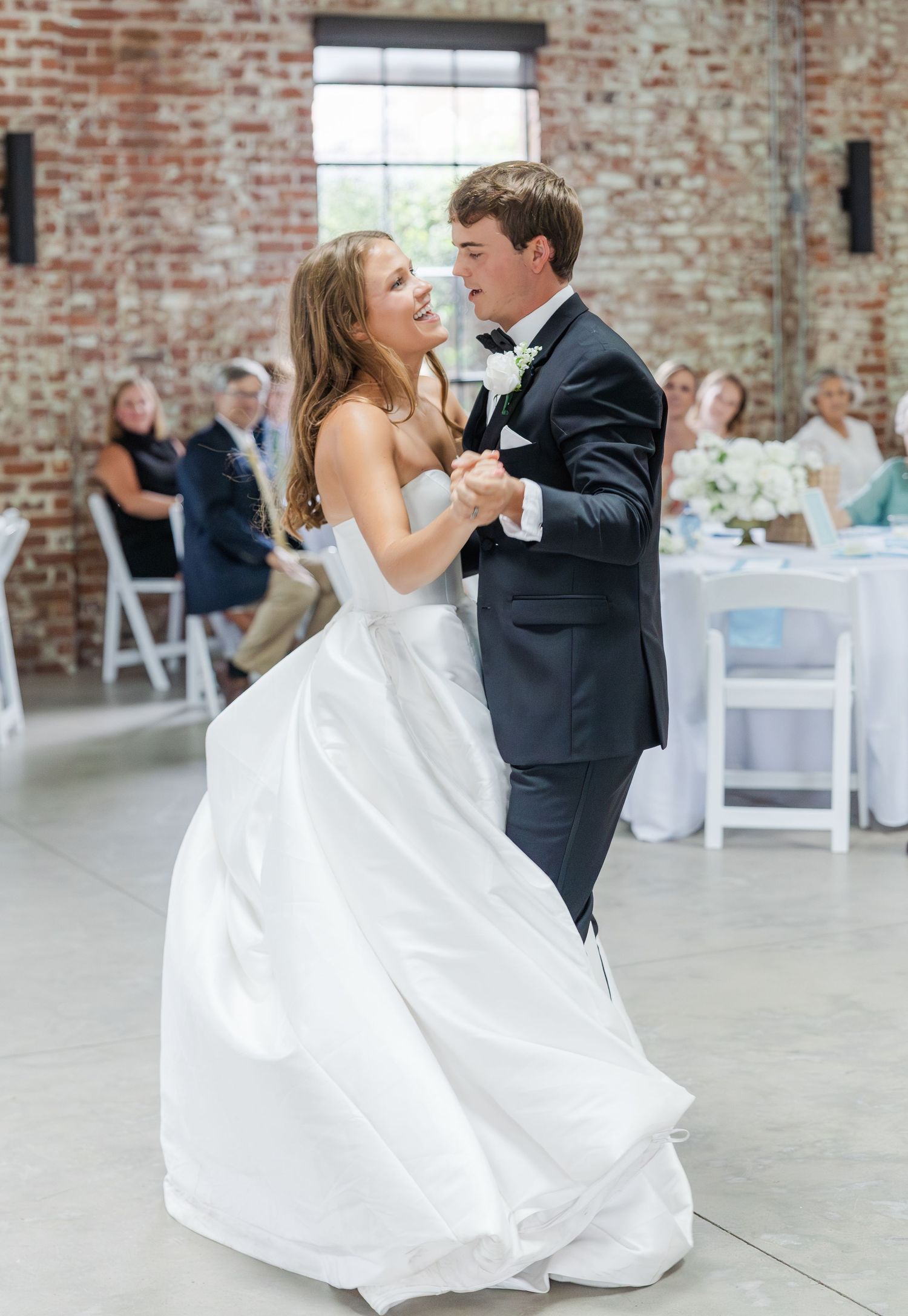 Bride and groom share their first dance in elegant venue with exposed brick walls.