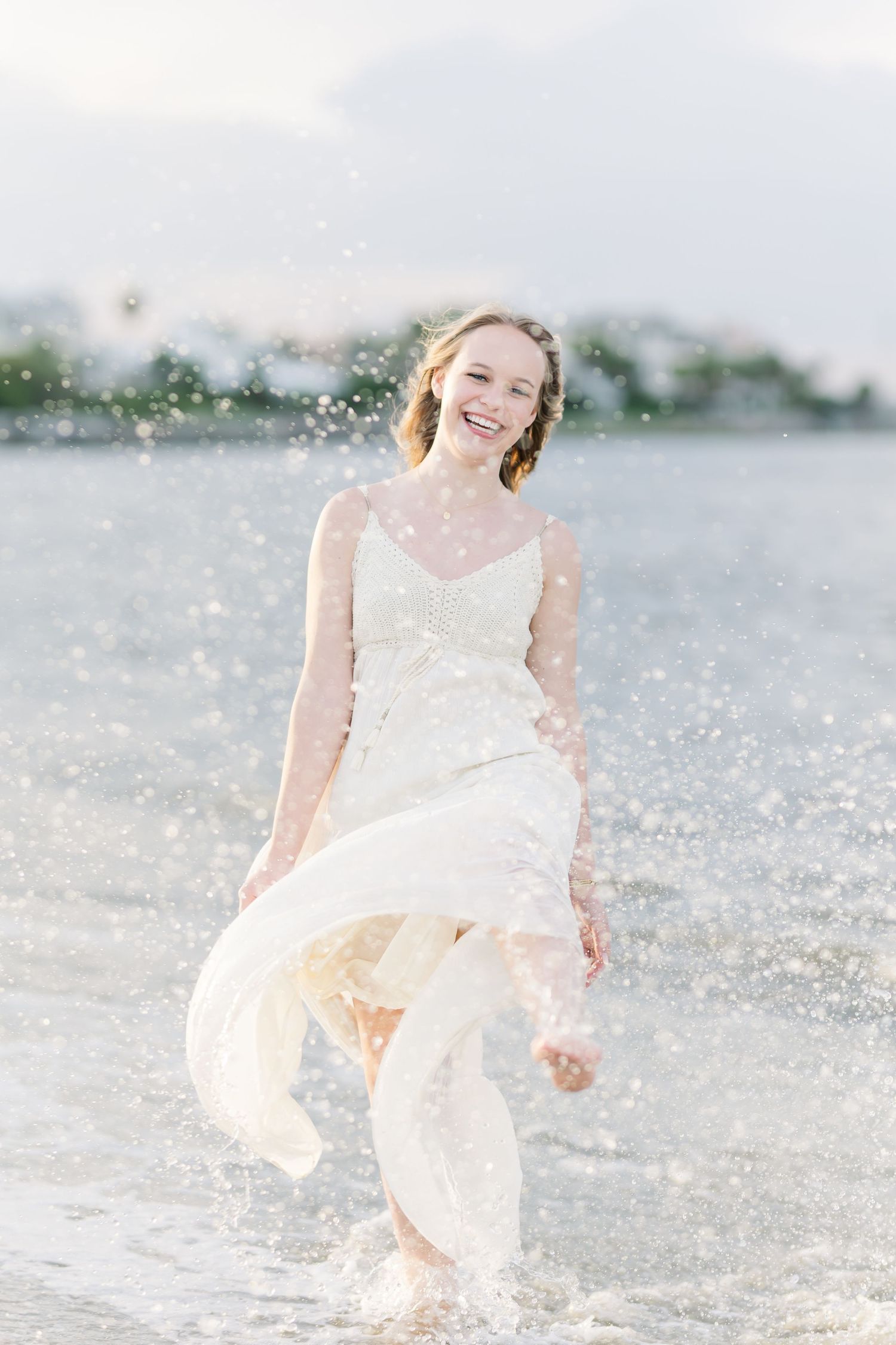 A joyful scene splashing in shallow water while wearing a flowing white dress at the beach.