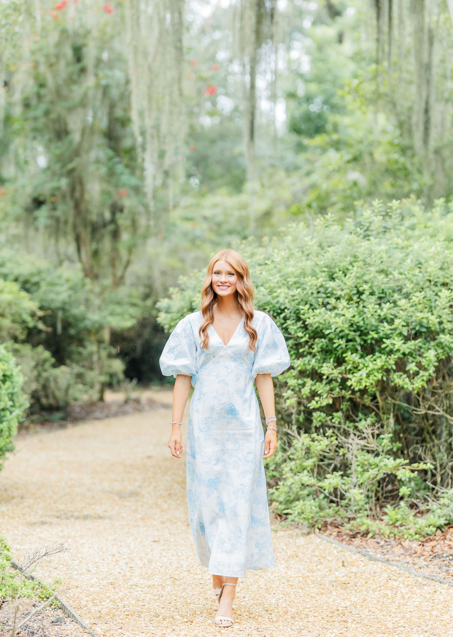 Light blue flowy summer dress with puff sleeves worn on a scenic path surrounded by green foliage and Spanish moss.