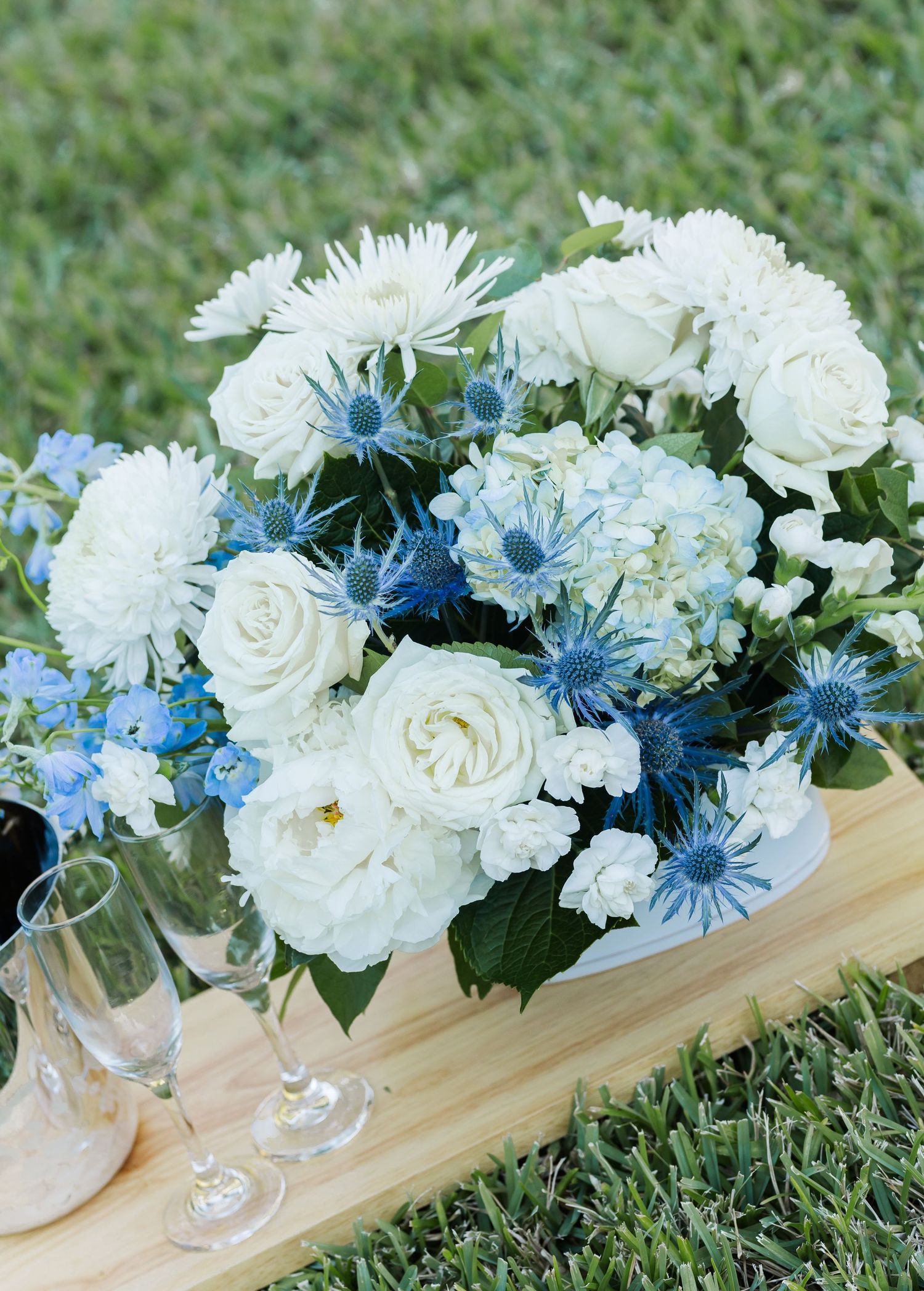 Rustic wooden box centerpiece filled with white carnations and blue daisies arranged on green grass.