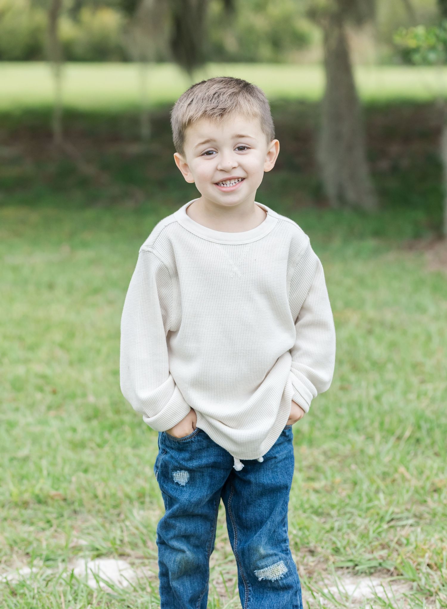 Young child in white sweater and jeans plays outdoors with joyful energy.