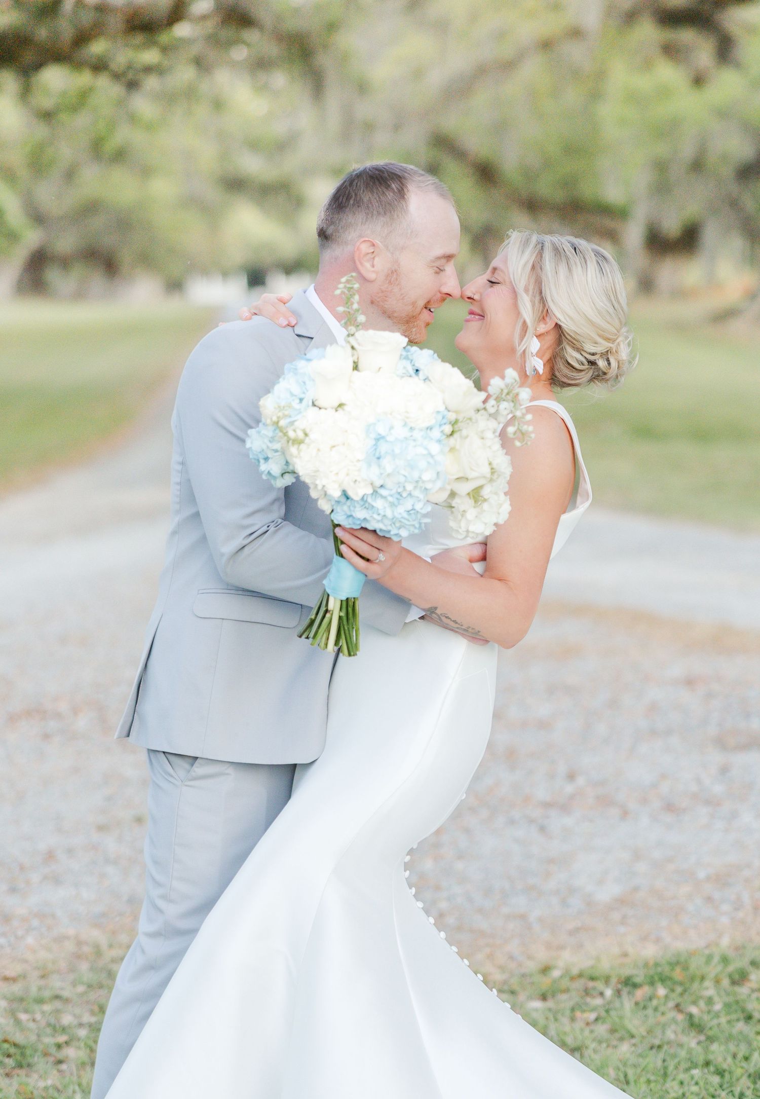 Bride and groom sharing a romantic moment, she holds a blue and white hydrangea bouquet outdoors.