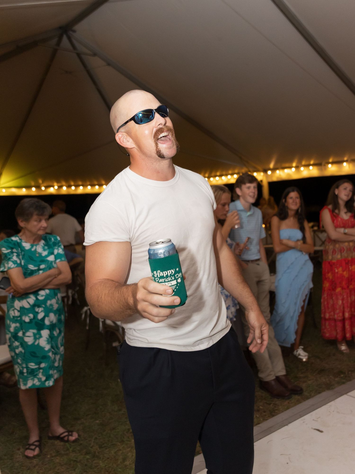 People dancing and celebrating at a wedding reception under a tent with string lights.