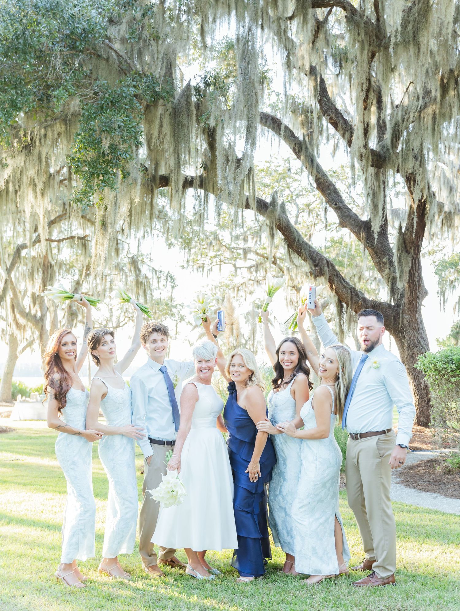 Bridal party in coordinated pastels celebrates joyfully under moss-covered oak trees.