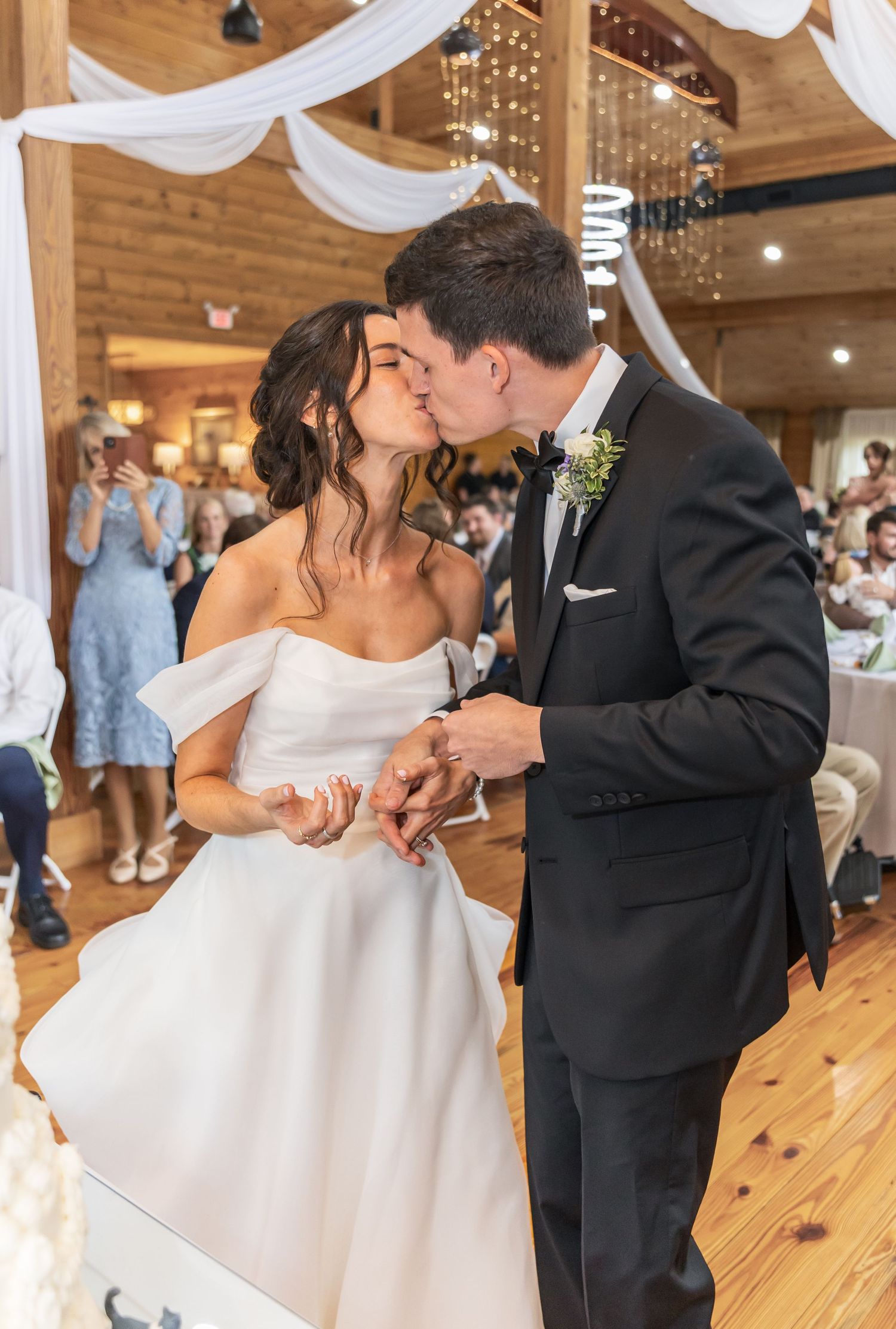 Newlyweds dancing romantically in a rustic reception hall with white drapery and string lights.