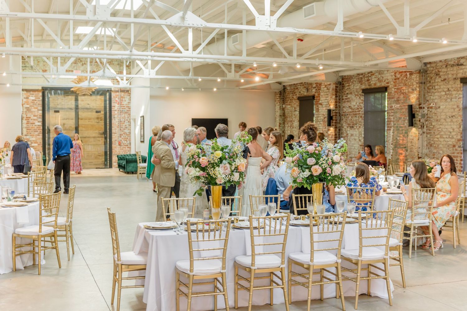 Elegant wedding reception venue with exposed brick walls, white chiavari chairs, and natural lighting through skylights.