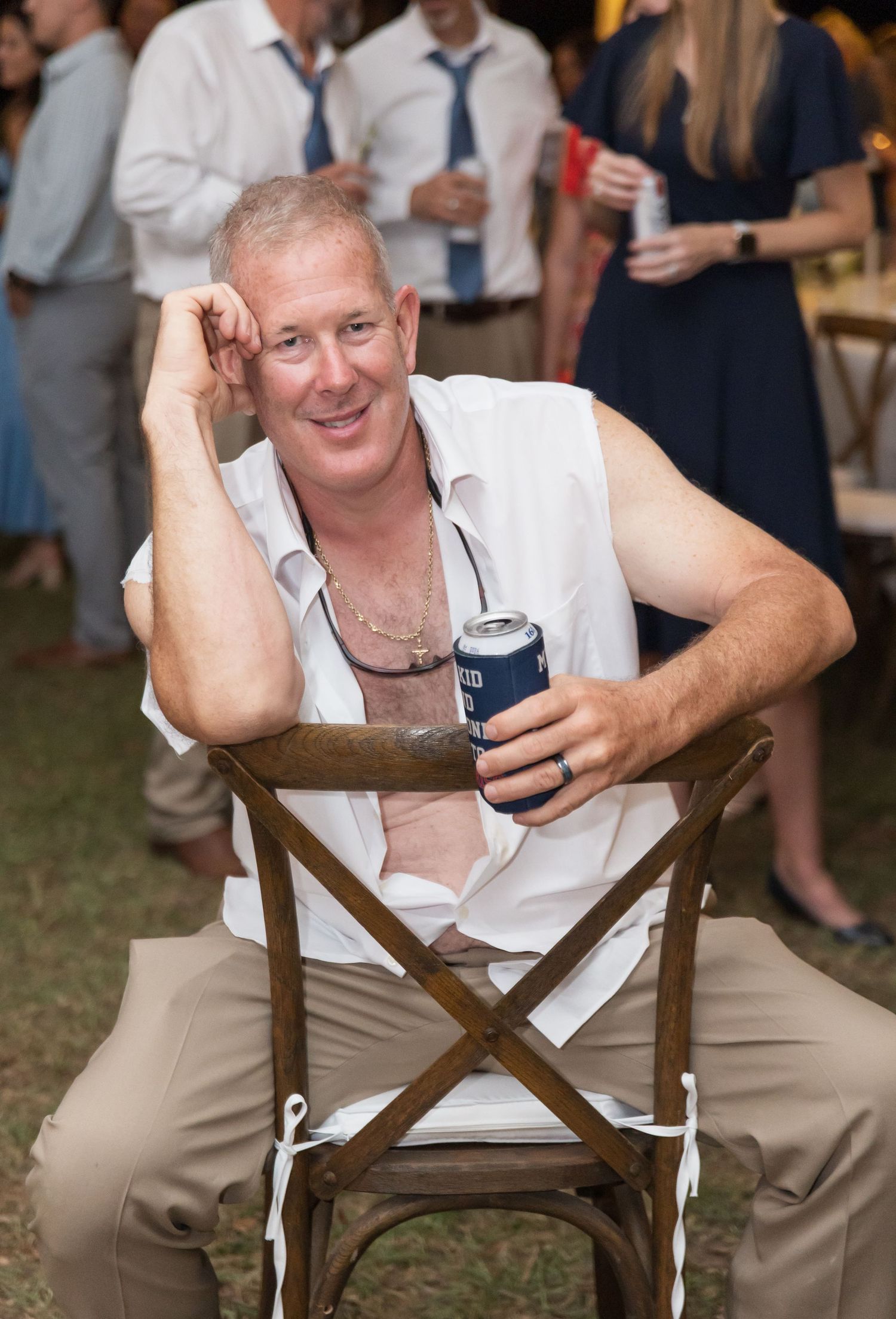 Guest relaxes in a wooden folding chair while enjoying a drink at an outdoor event.