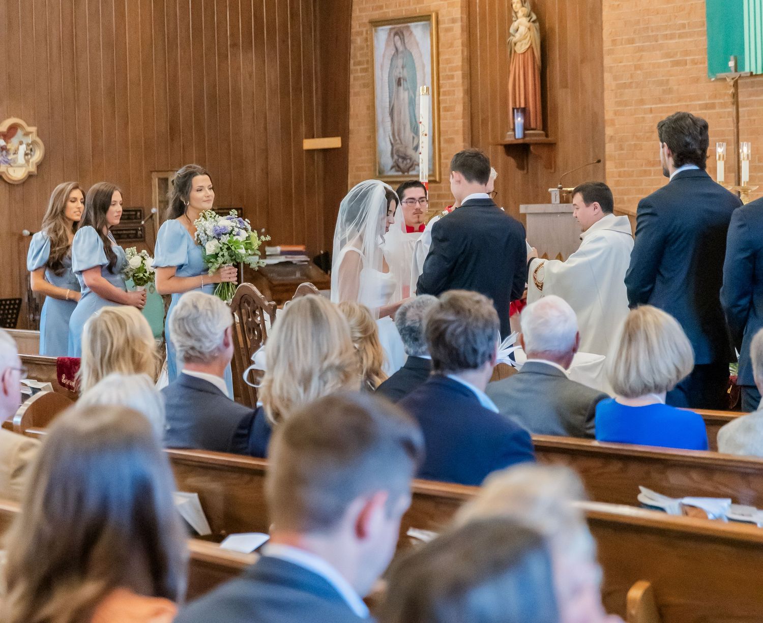 Wedding guests seated in wooden pews during a Catholic church ceremony.