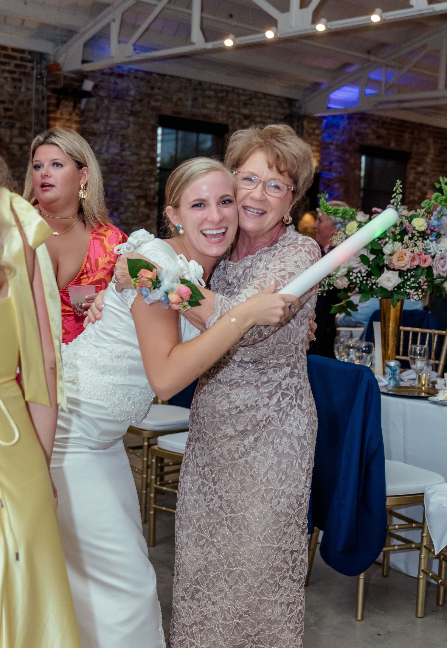 Guests celebrating with glow sticks during a wedding reception in a rustic brick venue.
