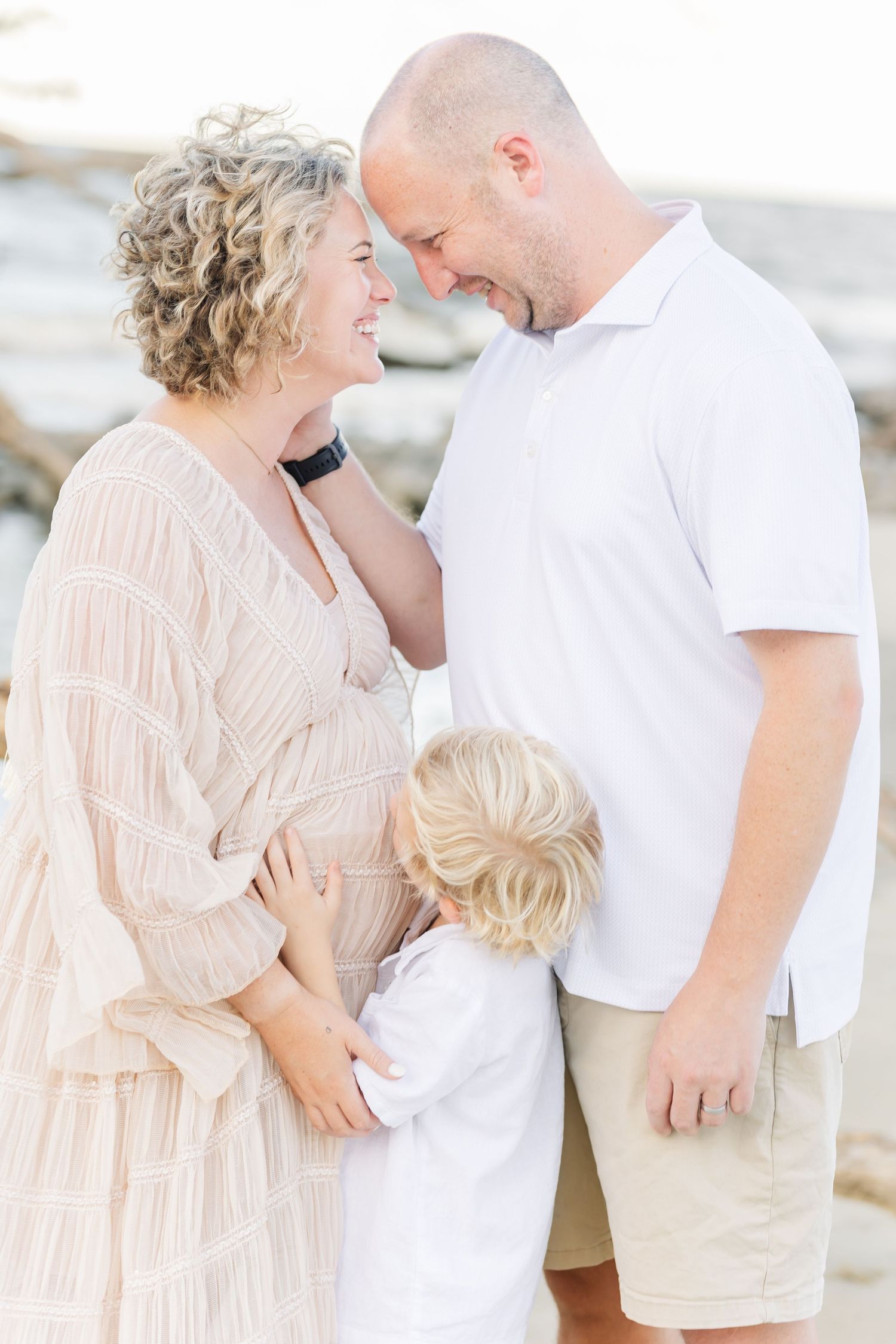 Romantic beach photoshoot with couple in peach dress and white shirt embracing near the ocean.